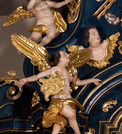 Zdjęcie nr 15: Nastawa architektoniczna, jednoosiowa, jednokondygnacyjna ze zwieńczeniem, ustawiona na wysokim cokole. Ołtarz drewniany, prostopadłościenny, o falistych bokach, mensa drewniana z marmurowym portatylem w drewnianej obudowie. Antepedium ujęte szeroką ramą dekorowaną płaskorzeźbionym motywem wieńca przepasanego wstęgą, w polu medalion z monogramem Marii ujęty wychodzącymi spod jego spodu wiązankami utworzonymi z suchego, wijącego się akantu z karbowaną wstęgą. Nastawa ujęta dwiema parami pilastrów, wewnętrzną z wolutowymi wspornikami w połowie wysokości trzonów oraz zewnętrzną parą o trzonach w formie spływów wolutowych przechodzących w silnie wysunięte do przodu partie cokołu, na których znajdują się postumenty dla figur aniołów. Podpory dźwigają niepełne belkowanie wyłamane na ich osi, nad polem środkowym wyłącznie gzyms przyjmujący kształt łuku półkolistego. Na belkowaniu fragmenty przerwanego, falistego przyczółka oraz para aniołów z kartuszami. W polu środkowym wnęka w formie stojącego prostokąta zamkniętego łukiem segmentowym nadwieszonym z uskokiem, w profilowanej ramie z mniejszym obrazem Matki Boskiej z Dzieciątkiem w kształcie stojącego prostokąta. Poniżej gablota na wota w formie leżącego prostokąta ujęta profilowaną ramą. Kondygnacja flankowana uszami utworzonymi z rocaille'u. Zwieńczenie w formie zbliżonej do kwadratu o wklęsłych bokach przechodzących w woluty, na których siedzą putta, zamknięte fragmentem falistego gzymsu wyłamanego po bokach, na nim rokokowy kartusz z monogramem IHS w polu, flankowany rocaille'em. W polu zwieńczenia rzeźba gołębicy Ducha Świętego w glorii promienistej i otoku z obłoków, w towarzystwie czterech uskrzydlonych główek anielskich. Wszystkie pilastry oraz łuki dekorowane elementami rocaille'u. Struktura w całości polichromowana na sposób imitujący marmoryzację w kolorze niebieskim, ornamentyka i profile złocone, detal srebrzony. 
Wewnątrz skrzyni ołtarzowej napisy „MALOWAŁ LUDWIK WÓJCIK Z KRAKOWA 2 / XI 1914”; „LUDWIK WÓJCIK”; „MALOWALI STOPY”; „23.02.1994 / KONSERWOWALI / KAZIMIERZ PATEJUK / EWA I JERZY SUCHWAŁKO / Z WARSZAWY / PROBOSZCZOWAŁ / KS. BOLESŁAW WAWAK”. 