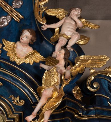 Zdjęcie nr 16: Nastawa architektoniczna, jednoosiowa, jednokondygnacyjna ze zwieńczeniem, ustawiona na wysokim cokole. Ołtarz drewniany, prostopadłościenny, o falistych bokach, mensa drewniana z marmurowym portatylem w drewnianej obudowie. Antepedium ujęte szeroką ramą dekorowaną płaskorzeźbionym motywem wieńca przepasanego wstęgą, w polu medalion z monogramem Marii ujęty wychodzącymi spod jego spodu wiązankami utworzonymi z suchego, wijącego się akantu z karbowaną wstęgą. Nastawa ujęta dwiema parami pilastrów, wewnętrzną z wolutowymi wspornikami w połowie wysokości trzonów oraz zewnętrzną parą o trzonach w formie spływów wolutowych przechodzących w silnie wysunięte do przodu partie cokołu, na których znajdują się postumenty dla figur aniołów. Podpory dźwigają niepełne belkowanie wyłamane na ich osi, nad polem środkowym wyłącznie gzyms przyjmujący kształt łuku półkolistego. Na belkowaniu fragmenty przerwanego, falistego przyczółka oraz para aniołów z kartuszami. W polu środkowym wnęka w formie stojącego prostokąta zamkniętego łukiem segmentowym nadwieszonym z uskokiem, w profilowanej ramie z mniejszym obrazem Matki Boskiej z Dzieciątkiem w kształcie stojącego prostokąta. Poniżej gablota na wota w formie leżącego prostokąta ujęta profilowaną ramą. Kondygnacja flankowana uszami utworzonymi z rocaille'u. Zwieńczenie w formie zbliżonej do kwadratu o wklęsłych bokach przechodzących w woluty, na których siedzą putta, zamknięte fragmentem falistego gzymsu wyłamanego po bokach, na nim rokokowy kartusz z monogramem IHS w polu, flankowany rocaille'em. W polu zwieńczenia rzeźba gołębicy Ducha Świętego w glorii promienistej i otoku z obłoków, w towarzystwie czterech uskrzydlonych główek anielskich. Wszystkie pilastry oraz łuki dekorowane elementami rocaille'u. Struktura w całości polichromowana na sposób imitujący marmoryzację w kolorze niebieskim, ornamentyka i profile złocone, detal srebrzony. 
Wewnątrz skrzyni ołtarzowej napisy „MALOWAŁ LUDWIK WÓJCIK Z KRAKOWA 2 / XI 1914”; „LUDWIK WÓJCIK”; „MALOWALI STOPY”; „23.02.1994 / KONSERWOWALI / KAZIMIERZ PATEJUK / EWA I JERZY SUCHWAŁKO / Z WARSZAWY / PROBOSZCZOWAŁ / KS. BOLESŁAW WAWAK”. 