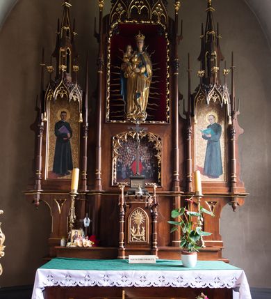 Zdjęcie nr 7: Nastawa ołtarzowa architektoniczna, trójosiowa, jednokondygnacyjna, z predellą. Ołtarz drewniany prostopadłościenny, z drewnianą mensą i portatylem z marmuru dębnickiego. W polu antepedium płycina ujęta blendami i maswerkiem; w centrum monogram Marii w wieńcu róż. Tabernakulum w formie prostopadłościennej skrzynki zamkniętej krenelażem, ujęte dwiema kolumienkami z pinaklami, z prostokątnymi drzwiczkami zamkniętymi łukiem ostrym z płaskorzeźbionym przedstawieniem kielicha, hostią w glorii, winną latoroślą i kłosami zbóż. Osie nastawy wydzielone smukłymi półkolumnami, zakończonymi pinaklami z kwiatonami. Oś środkowa dwukrotnie wyższa i szersza od bocznych. W polu środkowym nisza w formie stojącego prostokąta z figurą Matki Boskiej z Dzieciątkiem. Wnęka ujęta ramą dekorowaną ornamentem roślinnym. Poniżej płycina w kształcie kwadratu zamkniętego łukiem segmentowym, ujęta maswerkową ramą z przedstawieniem Chrystusa z więźniami obozu koncentracyjnego i duchownymi. Oś główna zamknięta baldachimem utworzonym z trzech wimperg oraz szczytem z pinakli i kwiatonów. Osie boczne z wnękami z obrazami bł. Stanisława Pyrtka i bł. Piotra Dańkowskiego, zwieńczonymi baldachimami utworzonymi z trzech wimperg i zakończonymi gotyckimi wieżyczkami. Struktura nastawy politurowana w kolorze jasnobrązowym, ornamentyka i detale architektoniczne złocone. 


