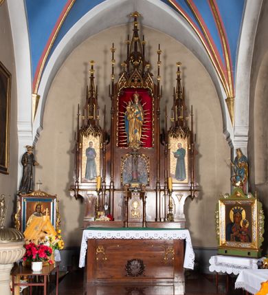 Zdjęcie nr 6: Nastawa ołtarzowa architektoniczna, trójosiowa, jednokondygnacyjna, z predellą. Ołtarz drewniany prostopadłościenny, z drewnianą mensą i portatylem z marmuru dębnickiego. W polu antepedium płycina ujęta blendami i maswerkiem; w centrum monogram Marii w wieńcu róż. Tabernakulum w formie prostopadłościennej skrzynki zamkniętej krenelażem, ujęte dwiema kolumienkami z pinaklami, z prostokątnymi drzwiczkami zamkniętymi łukiem ostrym z płaskorzeźbionym przedstawieniem kielicha, hostią w glorii, winną latoroślą i kłosami zbóż. Osie nastawy wydzielone smukłymi półkolumnami, zakończonymi pinaklami z kwiatonami. Oś środkowa dwukrotnie wyższa i szersza od bocznych. W polu środkowym nisza w formie stojącego prostokąta z figurą Matki Boskiej z Dzieciątkiem. Wnęka ujęta ramą dekorowaną ornamentem roślinnym. Poniżej płycina w kształcie kwadratu zamkniętego łukiem segmentowym, ujęta maswerkową ramą z przedstawieniem Chrystusa z więźniami obozu koncentracyjnego i duchownymi. Oś główna zamknięta baldachimem utworzonym z trzech wimperg oraz szczytem z pinakli i kwiatonów. Osie boczne z wnękami z obrazami bł. Stanisława Pyrtka i bł. Piotra Dańkowskiego, zwieńczonymi baldachimami utworzonymi z trzech wimperg i zakończonymi gotyckimi wieżyczkami. Struktura nastawy politurowana w kolorze jasnobrązowym, ornamentyka i detale architektoniczne złocone. 

