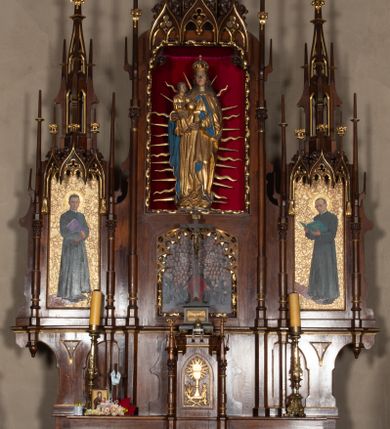 Zdjęcie nr 1: Nastawa ołtarzowa architektoniczna, trójosiowa, jednokondygnacyjna, z predellą. Ołtarz drewniany prostopadłościenny, z drewnianą mensą i portatylem z marmuru dębnickiego. W polu antepedium płycina ujęta blendami i maswerkiem; w centrum monogram Marii w wieńcu róż. Tabernakulum w formie prostopadłościennej skrzynki zamkniętej krenelażem, ujęte dwiema kolumienkami z pinaklami, z prostokątnymi drzwiczkami zamkniętymi łukiem ostrym z płaskorzeźbionym przedstawieniem kielicha, hostią w glorii, winną latoroślą i kłosami zbóż. Osie nastawy wydzielone smukłymi półkolumnami, zakończonymi pinaklami z kwiatonami. Oś środkowa dwukrotnie wyższa i szersza od bocznych. W polu środkowym nisza w formie stojącego prostokąta z figurą Matki Boskiej z Dzieciątkiem. Wnęka ujęta ramą dekorowaną ornamentem roślinnym. Poniżej płycina w kształcie kwadratu zamkniętego łukiem segmentowym, ujęta maswerkową ramą z przedstawieniem Chrystusa z więźniami obozu koncentracyjnego i duchownymi. Oś główna zamknięta baldachimem utworzonym z trzech wimperg oraz szczytem z pinakli i kwiatonów. Osie boczne z wnękami z obrazami bł. Stanisława Pyrtka i bł. Piotra Dańkowskiego, zwieńczonymi baldachimami utworzonymi z trzech wimperg i zakończonymi gotyckimi wieżyczkami. Struktura nastawy politurowana w kolorze jasnobrązowym, ornamentyka i detale architektoniczne złocone. 

