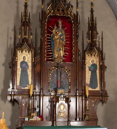 Zdjęcie nr 9: Nastawa ołtarzowa architektoniczna, trójosiowa, jednokondygnacyjna, z predellą. Ołtarz drewniany prostopadłościenny, z drewnianą mensą i portatylem z marmuru dębnickiego. W polu antepedium płycina ujęta blendami i maswerkiem; w centrum monogram Marii w wieńcu róż. Tabernakulum w formie prostopadłościennej skrzynki zamkniętej krenelażem, ujęte dwiema kolumienkami z pinaklami, z prostokątnymi drzwiczkami zamkniętymi łukiem ostrym z płaskorzeźbionym przedstawieniem kielicha, hostią w glorii, winną latoroślą i kłosami zbóż. Osie nastawy wydzielone smukłymi półkolumnami, zakończonymi pinaklami z kwiatonami. Oś środkowa dwukrotnie wyższa i szersza od bocznych. W polu środkowym nisza w formie stojącego prostokąta z figurą Matki Boskiej z Dzieciątkiem. Wnęka ujęta ramą dekorowaną ornamentem roślinnym. Poniżej płycina w kształcie kwadratu zamkniętego łukiem segmentowym, ujęta maswerkową ramą z przedstawieniem Chrystusa z więźniami obozu koncentracyjnego i duchownymi. Oś główna zamknięta baldachimem utworzonym z trzech wimperg oraz szczytem z pinakli i kwiatonów. Osie boczne z wnękami z obrazami bł. Stanisława Pyrtka i bł. Piotra Dańkowskiego, zwieńczonymi baldachimami utworzonymi z trzech wimperg i zakończonymi gotyckimi wieżyczkami. Struktura nastawy politurowana w kolorze jasnobrązowym, ornamentyka i detale architektoniczne złocone. 

