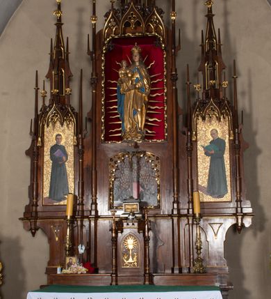 Zdjęcie nr 8: Nastawa ołtarzowa architektoniczna, trójosiowa, jednokondygnacyjna, z predellą. Ołtarz drewniany prostopadłościenny, z drewnianą mensą i portatylem z marmuru dębnickiego. W polu antepedium płycina ujęta blendami i maswerkiem; w centrum monogram Marii w wieńcu róż. Tabernakulum w formie prostopadłościennej skrzynki zamkniętej krenelażem, ujęte dwiema kolumienkami z pinaklami, z prostokątnymi drzwiczkami zamkniętymi łukiem ostrym z płaskorzeźbionym przedstawieniem kielicha, hostią w glorii, winną latoroślą i kłosami zbóż. Osie nastawy wydzielone smukłymi półkolumnami, zakończonymi pinaklami z kwiatonami. Oś środkowa dwukrotnie wyższa i szersza od bocznych. W polu środkowym nisza w formie stojącego prostokąta z figurą Matki Boskiej z Dzieciątkiem. Wnęka ujęta ramą dekorowaną ornamentem roślinnym. Poniżej płycina w kształcie kwadratu zamkniętego łukiem segmentowym, ujęta maswerkową ramą z przedstawieniem Chrystusa z więźniami obozu koncentracyjnego i duchownymi. Oś główna zamknięta baldachimem utworzonym z trzech wimperg oraz szczytem z pinakli i kwiatonów. Osie boczne z wnękami z obrazami bł. Stanisława Pyrtka i bł. Piotra Dańkowskiego, zwieńczonymi baldachimami utworzonymi z trzech wimperg i zakończonymi gotyckimi wieżyczkami. Struktura nastawy politurowana w kolorze jasnobrązowym, ornamentyka i detale architektoniczne złocone. 

