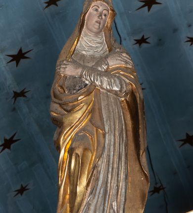 Zdjęcie nr 14: Belka tęczowa o falistym zarysie, zwieńczona profilowanym gzymsem. Z przodu napis „WSZYSCY KTÓRZY PRZYCHO/DZICIE OBACZCIE I UWAŻCIE: / OCZY MOJE BĘDĄ OTWARTE I USZY NACHYLONE NA PROŚBĘ TEGO KTÓRY SIĘ NA TEM MIEJSCU MODLIĆ BĘDZIE.”, na odwrociu napis „TEN KOŚCIÓŁ FUNDOWANY/ PRZEZ BARBARĘ LISICKĄ. / KONSEKROWANY W ROKU 1766. / ODNOMIONY W ROKU 1902. PO RAZ DRUGI W 1980”. Na belce ustawione figury ze sceny Ukrzyżowania. Pośrodku krzyż, do którego przybita jest trzema gwoździami figura umarłego Chrystusa. Ciało w lekkim zwisie o horyzontalnie rozłożonych ramionach, z głową opadającą na prawe ramię, z lekko ugiętymi nogami oraz stopami skrzyżowanymi w układzie prawa na lewą. Twarz ma szczupłą, o zamkniętych oczach, uniesionych brwiach, dużym, wąskim nosie oraz otwartych ustach, okoloną krótką, falowaną brodą i silnie kręconymi włosami opadającymi na ramiona. Na głowie ma koronę cierniową. Ciało jest wychudzone, o silnie zaznaczonych, guzowatych żebrach klatki piersiowej oraz mięśniach i ścięgnach ramion i ud. W partii bioder złocone perizonium zawieszone na sznurze, odsłaniające prawe udo, zawiązane ze zwisem tkaniny na prawym biodrze. 
U dołu krzyża klęczy Maria Magdalena, zwrócona w trzech czwartych w lewo, z uniesioną głową, obiema rękami obejmuje belkę. Twarz ma pociągłą, o małych oczach, krótkim nosie i wąskich ustach, okoloną długimi falowanymi włosami opadającymi na ramiona. Ubrana jest w srebrzoną suknię oraz złocony płaszcz. 
Po prawej stronie krzyża figura Marii, zwrócona w trzech czwartych w lewo, w kontrapoście, z pochyloną głową i rękami skrzyżowanymi na piersi. Twarz ma pociągłą, o wąskich oczach, uniesionych brwiach, małych nosie i ustach. Ubrana jest w srebrzoną suknię oraz złocony płaszcz narzucony na głowę i ramiona, wokół głowy ma białą podwikę. 
Po lewej stronie krzyża św. Jan zwrócony w trzech czwartych w prawo, w kontrapoście, prawą rękę kładzie na piersi, w lewej, opuszczonej trzyma księgę. Twarz ma pociągłą, o wąskich oczach, małych nosie i ustach, okoloną brązowymi, silnie kręconymi włosami, sięgającymi ramion, z czubem nad czołem. Ubrany jest w srebrzoną tunikę z kołnierzykiem, przepasaną w talii oraz złocony płaszcz zarzucony na prawe ramię i podtrzymywany na lewym boku. Polichromia ciał postaci naturalistyczna. 