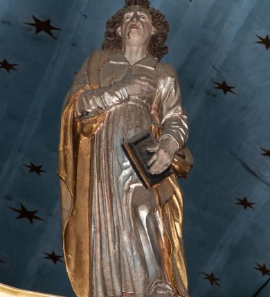 Zdjęcie nr 6: Belka tęczowa o falistym zarysie, zwieńczona profilowanym gzymsem. Z przodu napis „WSZYSCY KTÓRZY PRZYCHO/DZICIE OBACZCIE I UWAŻCIE: / OCZY MOJE BĘDĄ OTWARTE I USZY NACHYLONE NA PROŚBĘ TEGO KTÓRY SIĘ NA TEM MIEJSCU MODLIĆ BĘDZIE.”, na odwrociu napis „TEN KOŚCIÓŁ FUNDOWANY/ PRZEZ BARBARĘ LISICKĄ. / KONSEKROWANY W ROKU 1766. / ODNOMIONY W ROKU 1902. PO RAZ DRUGI W 1980”. Na belce ustawione figury ze sceny Ukrzyżowania. Pośrodku krzyż, do którego przybita jest trzema gwoździami figura umarłego Chrystusa. Ciało w lekkim zwisie o horyzontalnie rozłożonych ramionach, z głową opadającą na prawe ramię, z lekko ugiętymi nogami oraz stopami skrzyżowanymi w układzie prawa na lewą. Twarz ma szczupłą, o zamkniętych oczach, uniesionych brwiach, dużym, wąskim nosie oraz otwartych ustach, okoloną krótką, falowaną brodą i silnie kręconymi włosami opadającymi na ramiona. Na głowie ma koronę cierniową. Ciało jest wychudzone, o silnie zaznaczonych, guzowatych żebrach klatki piersiowej oraz mięśniach i ścięgnach ramion i ud. W partii bioder złocone perizonium zawieszone na sznurze, odsłaniające prawe udo, zawiązane ze zwisem tkaniny na prawym biodrze. 
U dołu krzyża klęczy Maria Magdalena, zwrócona w trzech czwartych w lewo, z uniesioną głową, obiema rękami obejmuje belkę. Twarz ma pociągłą, o małych oczach, krótkim nosie i wąskich ustach, okoloną długimi falowanymi włosami opadającymi na ramiona. Ubrana jest w srebrzoną suknię oraz złocony płaszcz. 
Po prawej stronie krzyża figura Marii, zwrócona w trzech czwartych w lewo, w kontrapoście, z pochyloną głową i rękami skrzyżowanymi na piersi. Twarz ma pociągłą, o wąskich oczach, uniesionych brwiach, małych nosie i ustach. Ubrana jest w srebrzoną suknię oraz złocony płaszcz narzucony na głowę i ramiona, wokół głowy ma białą podwikę. 
Po lewej stronie krzyża św. Jan zwrócony w trzech czwartych w prawo, w kontrapoście, prawą rękę kładzie na piersi, w lewej, opuszczonej trzyma księgę. Twarz ma pociągłą, o wąskich oczach, małych nosie i ustach, okoloną brązowymi, silnie kręconymi włosami, sięgającymi ramion, z czubem nad czołem. Ubrany jest w srebrzoną tunikę z kołnierzykiem, przepasaną w talii oraz złocony płaszcz zarzucony na prawe ramię i podtrzymywany na lewym boku. Polichromia ciał postaci naturalistyczna. 