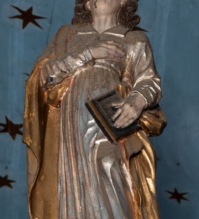 Zdjęcie nr 8: Belka tęczowa o falistym zarysie, zwieńczona profilowanym gzymsem. Z przodu napis „WSZYSCY KTÓRZY PRZYCHO/DZICIE OBACZCIE I UWAŻCIE: / OCZY MOJE BĘDĄ OTWARTE I USZY NACHYLONE NA PROŚBĘ TEGO KTÓRY SIĘ NA TEM MIEJSCU MODLIĆ BĘDZIE.”, na odwrociu napis „TEN KOŚCIÓŁ FUNDOWANY/ PRZEZ BARBARĘ LISICKĄ. / KONSEKROWANY W ROKU 1766. / ODNOMIONY W ROKU 1902. PO RAZ DRUGI W 1980”. Na belce ustawione figury ze sceny Ukrzyżowania. Pośrodku krzyż, do którego przybita jest trzema gwoździami figura umarłego Chrystusa. Ciało w lekkim zwisie o horyzontalnie rozłożonych ramionach, z głową opadającą na prawe ramię, z lekko ugiętymi nogami oraz stopami skrzyżowanymi w układzie prawa na lewą. Twarz ma szczupłą, o zamkniętych oczach, uniesionych brwiach, dużym, wąskim nosie oraz otwartych ustach, okoloną krótką, falowaną brodą i silnie kręconymi włosami opadającymi na ramiona. Na głowie ma koronę cierniową. Ciało jest wychudzone, o silnie zaznaczonych, guzowatych żebrach klatki piersiowej oraz mięśniach i ścięgnach ramion i ud. W partii bioder złocone perizonium zawieszone na sznurze, odsłaniające prawe udo, zawiązane ze zwisem tkaniny na prawym biodrze. 
U dołu krzyża klęczy Maria Magdalena, zwrócona w trzech czwartych w lewo, z uniesioną głową, obiema rękami obejmuje belkę. Twarz ma pociągłą, o małych oczach, krótkim nosie i wąskich ustach, okoloną długimi falowanymi włosami opadającymi na ramiona. Ubrana jest w srebrzoną suknię oraz złocony płaszcz. 
Po prawej stronie krzyża figura Marii, zwrócona w trzech czwartych w lewo, w kontrapoście, z pochyloną głową i rękami skrzyżowanymi na piersi. Twarz ma pociągłą, o wąskich oczach, uniesionych brwiach, małych nosie i ustach. Ubrana jest w srebrzoną suknię oraz złocony płaszcz narzucony na głowę i ramiona, wokół głowy ma białą podwikę. 
Po lewej stronie krzyża św. Jan zwrócony w trzech czwartych w prawo, w kontrapoście, prawą rękę kładzie na piersi, w lewej, opuszczonej trzyma księgę. Twarz ma pociągłą, o wąskich oczach, małych nosie i ustach, okoloną brązowymi, silnie kręconymi włosami, sięgającymi ramion, z czubem nad czołem. Ubrany jest w srebrzoną tunikę z kołnierzykiem, przepasaną w talii oraz złocony płaszcz zarzucony na prawe ramię i podtrzymywany na lewym boku. Polichromia ciał postaci naturalistyczna. 