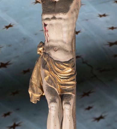 Zdjęcie nr 12: Belka tęczowa o falistym zarysie, zwieńczona profilowanym gzymsem. Z przodu napis „WSZYSCY KTÓRZY PRZYCHO/DZICIE OBACZCIE I UWAŻCIE: / OCZY MOJE BĘDĄ OTWARTE I USZY NACHYLONE NA PROŚBĘ TEGO KTÓRY SIĘ NA TEM MIEJSCU MODLIĆ BĘDZIE.”, na odwrociu napis „TEN KOŚCIÓŁ FUNDOWANY/ PRZEZ BARBARĘ LISICKĄ. / KONSEKROWANY W ROKU 1766. / ODNOMIONY W ROKU 1902. PO RAZ DRUGI W 1980”. Na belce ustawione figury ze sceny Ukrzyżowania. Pośrodku krzyż, do którego przybita jest trzema gwoździami figura umarłego Chrystusa. Ciało w lekkim zwisie o horyzontalnie rozłożonych ramionach, z głową opadającą na prawe ramię, z lekko ugiętymi nogami oraz stopami skrzyżowanymi w układzie prawa na lewą. Twarz ma szczupłą, o zamkniętych oczach, uniesionych brwiach, dużym, wąskim nosie oraz otwartych ustach, okoloną krótką, falowaną brodą i silnie kręconymi włosami opadającymi na ramiona. Na głowie ma koronę cierniową. Ciało jest wychudzone, o silnie zaznaczonych, guzowatych żebrach klatki piersiowej oraz mięśniach i ścięgnach ramion i ud. W partii bioder złocone perizonium zawieszone na sznurze, odsłaniające prawe udo, zawiązane ze zwisem tkaniny na prawym biodrze. 
U dołu krzyża klęczy Maria Magdalena, zwrócona w trzech czwartych w lewo, z uniesioną głową, obiema rękami obejmuje belkę. Twarz ma pociągłą, o małych oczach, krótkim nosie i wąskich ustach, okoloną długimi falowanymi włosami opadającymi na ramiona. Ubrana jest w srebrzoną suknię oraz złocony płaszcz. 
Po prawej stronie krzyża figura Marii, zwrócona w trzech czwartych w lewo, w kontrapoście, z pochyloną głową i rękami skrzyżowanymi na piersi. Twarz ma pociągłą, o wąskich oczach, uniesionych brwiach, małych nosie i ustach. Ubrana jest w srebrzoną suknię oraz złocony płaszcz narzucony na głowę i ramiona, wokół głowy ma białą podwikę. 
Po lewej stronie krzyża św. Jan zwrócony w trzech czwartych w prawo, w kontrapoście, prawą rękę kładzie na piersi, w lewej, opuszczonej trzyma księgę. Twarz ma pociągłą, o wąskich oczach, małych nosie i ustach, okoloną brązowymi, silnie kręconymi włosami, sięgającymi ramion, z czubem nad czołem. Ubrany jest w srebrzoną tunikę z kołnierzykiem, przepasaną w talii oraz złocony płaszcz zarzucony na prawe ramię i podtrzymywany na lewym boku. Polichromia ciał postaci naturalistyczna. 