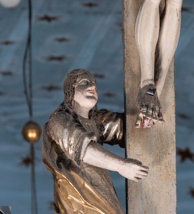 Zdjęcie nr 13: Belka tęczowa o falistym zarysie, zwieńczona profilowanym gzymsem. Z przodu napis „WSZYSCY KTÓRZY PRZYCHO/DZICIE OBACZCIE I UWAŻCIE: / OCZY MOJE BĘDĄ OTWARTE I USZY NACHYLONE NA PROŚBĘ TEGO KTÓRY SIĘ NA TEM MIEJSCU MODLIĆ BĘDZIE.”, na odwrociu napis „TEN KOŚCIÓŁ FUNDOWANY/ PRZEZ BARBARĘ LISICKĄ. / KONSEKROWANY W ROKU 1766. / ODNOMIONY W ROKU 1902. PO RAZ DRUGI W 1980”. Na belce ustawione figury ze sceny Ukrzyżowania. Pośrodku krzyż, do którego przybita jest trzema gwoździami figura umarłego Chrystusa. Ciało w lekkim zwisie o horyzontalnie rozłożonych ramionach, z głową opadającą na prawe ramię, z lekko ugiętymi nogami oraz stopami skrzyżowanymi w układzie prawa na lewą. Twarz ma szczupłą, o zamkniętych oczach, uniesionych brwiach, dużym, wąskim nosie oraz otwartych ustach, okoloną krótką, falowaną brodą i silnie kręconymi włosami opadającymi na ramiona. Na głowie ma koronę cierniową. Ciało jest wychudzone, o silnie zaznaczonych, guzowatych żebrach klatki piersiowej oraz mięśniach i ścięgnach ramion i ud. W partii bioder złocone perizonium zawieszone na sznurze, odsłaniające prawe udo, zawiązane ze zwisem tkaniny na prawym biodrze. 
U dołu krzyża klęczy Maria Magdalena, zwrócona w trzech czwartych w lewo, z uniesioną głową, obiema rękami obejmuje belkę. Twarz ma pociągłą, o małych oczach, krótkim nosie i wąskich ustach, okoloną długimi falowanymi włosami opadającymi na ramiona. Ubrana jest w srebrzoną suknię oraz złocony płaszcz. 
Po prawej stronie krzyża figura Marii, zwrócona w trzech czwartych w lewo, w kontrapoście, z pochyloną głową i rękami skrzyżowanymi na piersi. Twarz ma pociągłą, o wąskich oczach, uniesionych brwiach, małych nosie i ustach. Ubrana jest w srebrzoną suknię oraz złocony płaszcz narzucony na głowę i ramiona, wokół głowy ma białą podwikę. 
Po lewej stronie krzyża św. Jan zwrócony w trzech czwartych w prawo, w kontrapoście, prawą rękę kładzie na piersi, w lewej, opuszczonej trzyma księgę. Twarz ma pociągłą, o wąskich oczach, małych nosie i ustach, okoloną brązowymi, silnie kręconymi włosami, sięgającymi ramion, z czubem nad czołem. Ubrany jest w srebrzoną tunikę z kołnierzykiem, przepasaną w talii oraz złocony płaszcz zarzucony na prawe ramię i podtrzymywany na lewym boku. Polichromia ciał postaci naturalistyczna. 
