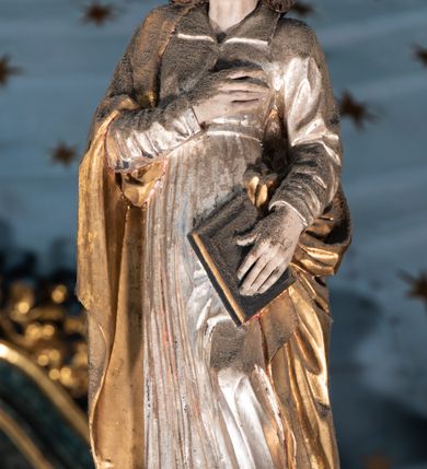 Zdjęcie nr 7: Belka tęczowa o falistym zarysie, zwieńczona profilowanym gzymsem. Z przodu napis „WSZYSCY KTÓRZY PRZYCHO/DZICIE OBACZCIE I UWAŻCIE: / OCZY MOJE BĘDĄ OTWARTE I USZY NACHYLONE NA PROŚBĘ TEGO KTÓRY SIĘ NA TEM MIEJSCU MODLIĆ BĘDZIE.”, na odwrociu napis „TEN KOŚCIÓŁ FUNDOWANY/ PRZEZ BARBARĘ LISICKĄ. / KONSEKROWANY W ROKU 1766. / ODNOMIONY W ROKU 1902. PO RAZ DRUGI W 1980”. Na belce ustawione figury ze sceny Ukrzyżowania. Pośrodku krzyż, do którego przybita jest trzema gwoździami figura umarłego Chrystusa. Ciało w lekkim zwisie o horyzontalnie rozłożonych ramionach, z głową opadającą na prawe ramię, z lekko ugiętymi nogami oraz stopami skrzyżowanymi w układzie prawa na lewą. Twarz ma szczupłą, o zamkniętych oczach, uniesionych brwiach, dużym, wąskim nosie oraz otwartych ustach, okoloną krótką, falowaną brodą i silnie kręconymi włosami opadającymi na ramiona. Na głowie ma koronę cierniową. Ciało jest wychudzone, o silnie zaznaczonych, guzowatych żebrach klatki piersiowej oraz mięśniach i ścięgnach ramion i ud. W partii bioder złocone perizonium zawieszone na sznurze, odsłaniające prawe udo, zawiązane ze zwisem tkaniny na prawym biodrze. 
U dołu krzyża klęczy Maria Magdalena, zwrócona w trzech czwartych w lewo, z uniesioną głową, obiema rękami obejmuje belkę. Twarz ma pociągłą, o małych oczach, krótkim nosie i wąskich ustach, okoloną długimi falowanymi włosami opadającymi na ramiona. Ubrana jest w srebrzoną suknię oraz złocony płaszcz. 
Po prawej stronie krzyża figura Marii, zwrócona w trzech czwartych w lewo, w kontrapoście, z pochyloną głową i rękami skrzyżowanymi na piersi. Twarz ma pociągłą, o wąskich oczach, uniesionych brwiach, małych nosie i ustach. Ubrana jest w srebrzoną suknię oraz złocony płaszcz narzucony na głowę i ramiona, wokół głowy ma białą podwikę. 
Po lewej stronie krzyża św. Jan zwrócony w trzech czwartych w prawo, w kontrapoście, prawą rękę kładzie na piersi, w lewej, opuszczonej trzyma księgę. Twarz ma pociągłą, o wąskich oczach, małych nosie i ustach, okoloną brązowymi, silnie kręconymi włosami, sięgającymi ramion, z czubem nad czołem. Ubrany jest w srebrzoną tunikę z kołnierzykiem, przepasaną w talii oraz złocony płaszcz zarzucony na prawe ramię i podtrzymywany na lewym boku. Polichromia ciał postaci naturalistyczna. 