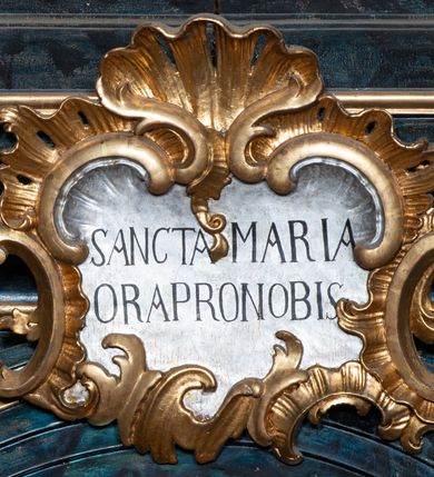 Zdjęcie nr 26: Nastawa architektoniczna, jednoosiowa, jednokondygnacyjna ze zwieńczeniem. Ołtarz prostopadłościenny, murowany, w drewnianej obudowie, z kamienną mensą. 
Antepedium ujęte profilowaną ramą, w polu malowana płycina w formie leżącego prostokąta o wklęsłych narożach, wypełniona wicią roślinną z różami, z kartuszem w centrum. W narożach przedstawienia ptaków na gałęziach. W polu kartusza ukazana półpostać Matki Boskiej Szkaplerznej unoszącej się nad duszami czyśćcowymi, na tle nieba. Retabulum ustawione na wysokim cokole, szerszym od nastawy, z wyłamanymi czterema prostopadłościanami. Nastawa ujęta parą zdwojonych pilastrów i parą stojących przed nimi kolumn o kapitelach kompozytowych, dźwigających pełne belkowanie, wyłamane na ich osi, z architrawem przyjmującym nad polem środkowym formę łuku odcinkowego. Na belkowaniu fragmenty półkolistego, przerwanego przyczółka z siedzącymi puttami. W polu centralnym wnęka w formie stojącego prostokąta zamkniętego łukiem półkolistym nadwieszonym z uskokiem, ujęta profilowaną ramą, z mniejszym obrazem Matki Boskiej z Dzieciątkiem w kształcie stojącego prostokąta. Powyżej, w podłuczu monogram Marii. Nad wnęką, w polu belkowania rocaille'owy kartusz z napisem „SANCTA MARIA / ORA PRO NOBIS”. Na skrajnych partiach cokołu ustawione figury św. Joachima i św. Józefa. Zwieńczenie w formie zbliżonej do trapezu, ujętego spływami wolutowymi, zamkniętego fragmentem gzymsu w formie łuku półkolistego nadwieszonego. Flankowane liśćmi palmowymi, gzyms dekorowany rocaille'm. W polu obraz Matki Boskiej Szkaplerznej ze św. Szymonem Stockiem i św. Teresą z Avili w formie analogicznej do zwieńczenia, w profilowanej ramie. Struktura polichromowana na sposób imitujący marmoryzację w kolorze niebiesko-czarnym, profile i ornamentyka złocone, detal srebrzony. 


