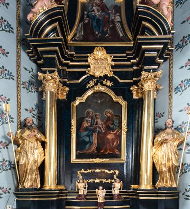 Zdjęcie nr 1: Nastawa architektoniczna, jednoosiowa, jednokondygnacyjna ze zwieńczeniem. Ołtarz prostopadłościenny, murowany, w drewnianej obudowie, z kamienną mensą. 
Antepedium ujęte profilowaną ramą, w polu malowana płycina w formie leżącego prostokąta o wklęsłych narożach, wypełniona wicią roślinną z różami, z kartuszem w centrum. W narożach przedstawienia ptaków na gałęziach. W polu kartusza ukazana półpostać Matki Boskiej Szkaplerznej unoszącej się nad duszami czyśćcowymi, na tle nieba. Retabulum ustawione na wysokim cokole, szerszym od nastawy, z wyłamanymi czterema prostopadłościanami. Nastawa ujęta parą zdwojonych pilastrów i parą stojących przed nimi kolumn o kapitelach kompozytowych, dźwigających pełne belkowanie, wyłamane na ich osi, z architrawem przyjmującym nad polem środkowym formę łuku odcinkowego. Na belkowaniu fragmenty półkolistego, przerwanego przyczółka z siedzącymi puttami. W polu centralnym wnęka w formie stojącego prostokąta zamkniętego łukiem półkolistym nadwieszonym z uskokiem, ujęta profilowaną ramą, z mniejszym obrazem Matki Boskiej z Dzieciątkiem w kształcie stojącego prostokąta. Powyżej, w podłuczu monogram Marii. Nad wnęką, w polu belkowania rocaille'owy kartusz z napisem „SANCTA MARIA / ORA PRO NOBIS”. Na skrajnych partiach cokołu ustawione figury św. Joachima i św. Józefa. Zwieńczenie w formie zbliżonej do trapezu, ujętego spływami wolutowymi, zamkniętego fragmentem gzymsu w formie łuku półkolistego nadwieszonego. Flankowane liśćmi palmowymi, gzyms dekorowany rocaille'm. W polu obraz Matki Boskiej Szkaplerznej ze św. Szymonem Stockiem i św. Teresą z Avili w formie analogicznej do zwieńczenia, w profilowanej ramie. Struktura polichromowana na sposób imitujący marmoryzację w kolorze niebiesko-czarnym, profile i ornamentyka złocone, detal srebrzony. 


