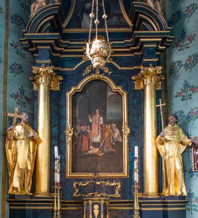 Zdjęcie nr 1: Nastawa architektoniczna, jednoosiowa, jednokondygnacyjna ze zwieńczeniem. Ołtarz prostopadłościenny, murowany, w drewnianej obudowie, z kamienną mensą. 
Antepedium ujęte profilowaną ramą, w polu malowana płycina w formie leżącego prostokąta o wklęsłych narożach, wypełniona wicią roślinną z różami, z kartuszem w centrum. W narożach przedstawienia ptaków na gałęziach. W polu kartusza scena męczeństwa św. Walentego, na tle pejzażu. Retabulum ustawione na wysokim cokole, szerszym od nastawy, z wyłamanymi czterema prostopadłościanami. Nastawa ujęta parą zdwojonych pilastrów i parą stojących przed nimi kolumn o kapitelach kompozytowych, dźwigających pełne belkowanie, wyłamane na ich osi, z architrawem przyjmującym nad polem środkowym formę łuku odcinkowego. Na belkowaniu fragmenty półkolistego, przerwanego przyczółka z siedzącymi puttami. W polu centralnym wnęka w formie stojącego prostokąta zamkniętego łukiem półkolistym nadwieszonym z uskokiem, ujęta profilowaną ramą, z obrazem św. Walentego. Nad nią, w polu belkowania rocaille&#039;owy kartusz z napisem „GLORIA HONORE / CORONASTI EUM / DOMINE”. Na skrajnych partiach cokołu ustawione figury św. Jana od Krzyża i św. Jana Kapistrana (?). Zwieńczenie w formie zbliżonej do trapezu, ujętego spływami wolutowymi, zamkniętego fragmentem gzymsu w formie łuku półkolistego nadwieszonego. Zwieńczenie flankowane liśćmi palmowymi, gzyms dekorowany rocaille&#039;m. W polu obraz św. Jana Nepomucena w kształcie analogicznym do zwieńczenia, w profilowanej ramie. Struktura polichromowana na sposób imitujący marmoryzację w kolorze niebieskim, profile i ornamentyka złocone, detal srebrzony. 

