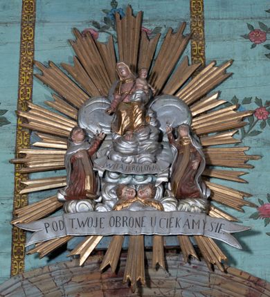 Zdjęcie nr 1: Na tle srebrzonych obłoków przedstawienie tronującej Matki Boskiej z Dzieciątkiem, flankowanej przez klęczące postacie świętych. Maria ukazana jako siedząca, frontalnie, przechylona w prawo, z prawą ręką wyciągniętą w dół oraz lewą podtrzymującą Dzieciątko. Ubrana jest w różową suknię, przepasaną w talii oraz złocony welon i złocony płaszcz, opadający na kolana. Dzieciątko w pozycji siedzącej, zwrócone w lewo, pochylone, obie ręce ma ugięte. Przewiązane jest srebrzoną pieluszką. Po prawej stronie Marii klęczy św. Szymon Stock, zwrócony w trzech czwartych w lewo, z uniesioną głową, odchylony w tył, prawą rękę kładzie na piersi, lewą wyciąga w górę. Twarz ma pełną, na głowie ma tonsurę. Ubrany jest w brązowy habit, ze złoconym szkaplerzem i srebrzonym płaszczem z kapturem. Po lewej stronie klęczy św. Maria Magdalena de Pazzi, zwrócona w trzech czwartych w prawo, z uniesioną głową, lewą rękę ma opuszczoną wzdłuż boku, prawą wyciąga w górę. Ubrana jest w brązowy habit, ze złoconym szkaplerzem oraz w srebrzony welon i płaszcz, na głowie ma zieloną koronę cierniową. U stóp Matki Boskiej, na tle obłoków banderola z napisem „WITAJ KRÓLOWA”, pod nim zaś dwie uskrzydlone główki anielskie. Poniżej całej sceny srebrzona banderola z napisem „POD TWOJA OBRONE UCIEKAMY SIE”. Całość w złoconej glorii promienistej. Polichromia ciał postaci naturalistyczna. 