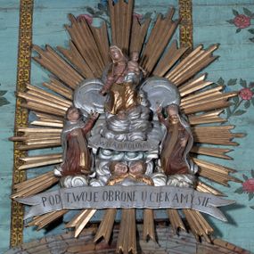 Zdjęcie nr 1: Na tle srebrzonych obłoków przedstawienie tronującej Matki Boskiej z Dzieciątkiem, flankowanej przez klęczące postacie świętych. Maria ukazana jako siedząca, frontalnie, przechylona w prawo, z prawą ręką wyciągniętą w dół oraz lewą podtrzymującą Dzieciątko. Ubrana jest w różową suknię, przepasaną w talii oraz złocony welon i złocony płaszcz, opadający na kolana. Dzieciątko w pozycji siedzącej, zwrócone w lewo, pochylone, obie ręce ma ugięte. Przewiązane jest srebrzoną pieluszką. Po prawej stronie Marii klęczy św. Szymon Stock, zwrócony w trzech czwartych w lewo, z uniesioną głową, odchylony w tył, prawą rękę kładzie na piersi, lewą wyciąga w górę. Twarz ma pełną, na głowie ma tonsurę. Ubrany jest w brązowy habit, ze złoconym szkaplerzem i srebrzonym płaszczem z kapturem. Po lewej stronie klęczy św. Maria Magdalena de Pazzi, zwrócona w trzech czwartych w prawo, z uniesioną głową, lewą rękę ma opuszczoną wzdłuż boku, prawą wyciąga w górę. Ubrana jest w brązowy habit, ze złoconym szkaplerzem oraz w srebrzony welon i płaszcz, na głowie ma zieloną koronę cierniową. U stóp Matki Boskiej, na tle obłoków banderola z napisem „WITAJ KRÓLOWA”, pod nim zaś dwie uskrzydlone główki anielskie. Poniżej całej sceny srebrzona banderola z napisem „POD TWOJA OBRONE UCIEKAMY SIE”. Całość w złoconej glorii promienistej. Polichromia ciał postaci naturalistyczna. 