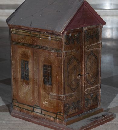 Zdjęcie nr 1: Tabernakulum w formie drewnianej skrzynki, zamkniętej trójbocznie, imitującej budynek, przykrytej wielospadowym dachem, na profilowanym cokole. Drzwiczki dwuskrzydłowe, w kształcie stojącego prostokąta, zwieńczone trójkątnym szczytem, zamocowane na zawiasach z okuciami. Dekorowane malowanymi płycinami o fantazyjnym kształcie i ornamentem.  Ścianki boczne z malowaną architekturą w kolorze jasnobrązowym, dwuosiowe, wydzielone pilastrami dźwigającymi belkowanie. Na osiach malowane okienka w dekoracyjnych opaskach. Na tylnej ściance namalowane belkowanie oraz dwie połówki okien w dekoracyjnych opaskach. Wnętrze tabernakulum polichromowane w kolorze jasnoniebieskim ze złoconymi gwiazdami. Drzwiczki po wewnętrznej stronie z malowaną dekoracją w postaci cokołów z wazonami i kwiatami, na jasnoniebieskim tle, w górnej partii ornament. 
