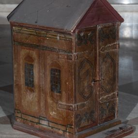 Zdjęcie nr 1: Tabernakulum w formie drewnianej skrzynki, zamkniętej trójbocznie, imitującej budynek, przykrytej wielospadowym dachem, na profilowanym cokole. Drzwiczki dwuskrzydłowe, w kształcie stojącego prostokąta, zwieńczone trójkątnym szczytem, zamocowane na zawiasach z okuciami. Dekorowane malowanymi płycinami o fantazyjnym kształcie i ornamentem.  Ścianki boczne z malowaną architekturą w kolorze jasnobrązowym, dwuosiowe, wydzielone pilastrami dźwigającymi belkowanie. Na osiach malowane okienka w dekoracyjnych opaskach. Na tylnej ściance namalowane belkowanie oraz dwie połówki okien w dekoracyjnych opaskach. Wnętrze tabernakulum polichromowane w kolorze jasnoniebieskim ze złoconymi gwiazdami. Drzwiczki po wewnętrznej stronie z malowaną dekoracją w postaci cokołów z wazonami i kwiatami, na jasnoniebieskim tle, w górnej partii ornament. 
