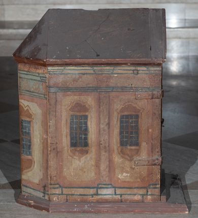 Zdjęcie nr 3: Tabernakulum w formie drewnianej skrzynki, zamkniętej trójbocznie, imitującej budynek, przykrytej wielospadowym dachem, na profilowanym cokole. Drzwiczki dwuskrzydłowe, w kształcie stojącego prostokąta, zwieńczone trójkątnym szczytem, zamocowane na zawiasach z okuciami. Dekorowane malowanymi płycinami o fantazyjnym kształcie i ornamentem.  Ścianki boczne z malowaną architekturą w kolorze jasnobrązowym, dwuosiowe, wydzielone pilastrami dźwigającymi belkowanie. Na osiach malowane okienka w dekoracyjnych opaskach. Na tylnej ściance namalowane belkowanie oraz dwie połówki okien w dekoracyjnych opaskach. Wnętrze tabernakulum polichromowane w kolorze jasnoniebieskim ze złoconymi gwiazdami. Drzwiczki po wewnętrznej stronie z malowaną dekoracją w postaci cokołów z wazonami i kwiatami, na jasnoniebieskim tle, w górnej partii ornament. 
