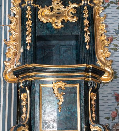 Zdjęcie nr 3: Ambona przyścienna, wisząca, z dostępem przez drzwi w zaplecku, od strony zakrystii. Kosz na planie kwadratu o wklęsłych ściankach i ściętych narożach, na podstawie w postaci wałka dekorowanego rocaille’m, z podwieszeniem w formie zbliżonej do stożka zakończonego szyszką, w którego ściętych narożach znajdują się spływy wolutowe dekorowane kampanulami i pola ozdobione rocaille’m. Kosz w narożach ujęty pilastrami o trzonach przechodzących w spływy wolutowe, dekorowanych kampanulami i rocaille’m, dźwigających niepełne belkowanie stanowiące parapet. Ścianki kosza zdobione płycinami z rocaille’m. Zaplecek ujęty pilastrami o kanelowanych trzonach, zakończonymi konsolami z podwieszonymi kampanulami, dźwigającymi imposty oraz fragmenty, przerwanego, wolutowego przyczółka. Pomiędzy nimi, w polu zwieńczenia gołębica Ducha Świętego w otoku z obłoków, w glorii promienistej. W polu zaplecka drzwi, ponad nimi rocaille. Zaplecek ujęty uszami utworzonymi ze spływów wolutowych, liści palmowych i kwiatów. Struktura polichromowana na sposób imitujący marmoryzację w kolorze ciemnej zieleni ze złoconymi profilami i ornamentyką, gołębica srebrzona. 