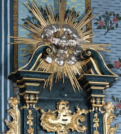 Zdjęcie nr 10: Ambona przyścienna, wisząca, z dostępem przez drzwi w zaplecku, od strony zakrystii. Kosz na planie kwadratu o wklęsłych ściankach i ściętych narożach, na podstawie w postaci wałka dekorowanego rocaille’m, z podwieszeniem w formie zbliżonej do stożka zakończonego szyszką, w którego ściętych narożach znajdują się spływy wolutowe dekorowane kampanulami i pola ozdobione rocaille’m. Kosz w narożach ujęty pilastrami o trzonach przechodzących w spływy wolutowe, dekorowanych kampanulami i rocaille’m, dźwigających niepełne belkowanie stanowiące parapet. Ścianki kosza zdobione płycinami z rocaille’m. Zaplecek ujęty pilastrami o kanelowanych trzonach, zakończonymi konsolami z podwieszonymi kampanulami, dźwigającymi imposty oraz fragmenty, przerwanego, wolutowego przyczółka. Pomiędzy nimi, w polu zwieńczenia gołębica Ducha Świętego w otoku z obłoków, w glorii promienistej. W polu zaplecka drzwi, ponad nimi rocaille. Zaplecek ujęty uszami utworzonymi ze spływów wolutowych, liści palmowych i kwiatów. Struktura polichromowana na sposób imitujący marmoryzację w kolorze ciemnej zieleni ze złoconymi profilami i ornamentyką, gołębica srebrzona. 
