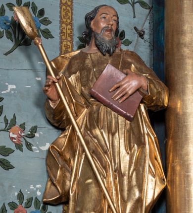 Zdjęcie nr 1: Rzeźba ścięta i drążona z tyłu, ustawiona na niskiej podstawie. Święty zwrócony frontalnie, w kontrapoście, z przechyloną łukowato sylwetką i głową skierowaną delikatnie w lewo. Lewą ręką przyciska do piersi księgę, w prawej, ugiętej trzyma szuflę pasterską. Twarz ma pociągłą, szczupłą, z wysokim czołem, o małych oczach skierowanych w górę, z głęboko rzeźbioną górną powieką, o dużym nosie i pełnych ustach o szerokiej górnej wardze. Twarz okolona kręconą, rozdwajającą się brodą oraz włosami o grubych falach opadającymi na ramiona. Ubrany jest w długą tunikę o wąskich rękawach, przepasaną w talii, przylegającą do ciała. Przez prawe ramię ma przerzucony silnie drapowany płaszcz, opadający na plecy i na prawy bok postaci. Polichromia ciała naturalistyczna, szaty i atrybut złocone.