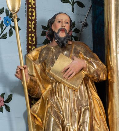 Zdjęcie nr 6: Rzeźba ścięta i drążona z tyłu, ustawiona na niskiej podstawie. Święty zwrócony frontalnie, w kontrapoście, z przechyloną łukowato sylwetką i głową skierowaną delikatnie w lewo. Lewą ręką przyciska do piersi księgę, w prawej, ugiętej trzyma szuflę pasterską. Twarz ma pociągłą, szczupłą, z wysokim czołem, o małych oczach skierowanych w górę, z głęboko rzeźbioną górną powieką, o dużym nosie i pełnych ustach o szerokiej górnej wardze. Twarz okolona kręconą, rozdwajającą się brodą oraz włosami o grubych falach opadającymi na ramiona. Ubrany jest w długą tunikę o wąskich rękawach, przepasaną w talii, przylegającą do ciała. Przez prawe ramię ma przerzucony silnie drapowany płaszcz, opadający na plecy i na prawy bok postaci. Polichromia ciała naturalistyczna, szaty i atrybut złocone.