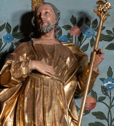 Zdjęcie nr 1: Rzeźba ścięta z tyłu, drążona, ustawiona na niskiej podstawie. Święty ukazany frontalnie, w kontrapoście, o lekko przechylonej sylwetce i głowie skierowanej w trzech czwartych w prawo. W lewej, ugiętej ręce trzyma laskę zakończoną lilią, prawą kładzie na piersi. Twarz ma pociągłą, szczupłą, o małych oczach, skierowanych do góry, z głęboko rzeźbioną powieką, dużym nosie i pełnych ustach o szerokiej górnej wardze. Twarz okolona krótką, kręconą brodą oraz siwymi włosami, opadającymi falistymi puklami na ramiona. Ubrany jest w długą suknię o wąskich rękawach, przepasaną w talii, przylegającą do ciała. Przez lewe ramię ma przerzucony silnie fałdowany płaszcz, opadający na plecy i po bokach postaci. Polichromia naturalistyczna w partiach ciała, szaty i atrybut złocone.