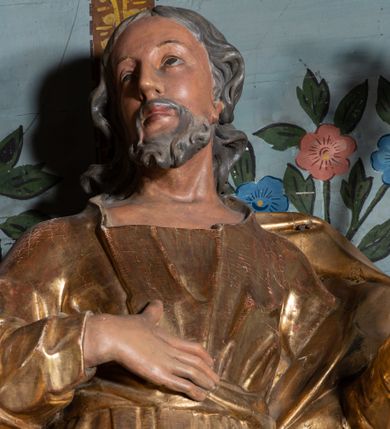 Zdjęcie nr 6: Rzeźba ścięta z tyłu, drążona, ustawiona na niskiej podstawie. Święty ukazany frontalnie, w kontrapoście, o lekko przechylonej sylwetce i głowie skierowanej w trzech czwartych w prawo. W lewej, ugiętej ręce trzyma laskę zakończoną lilią, prawą kładzie na piersi. Twarz ma pociągłą, szczupłą, o małych oczach, skierowanych do góry, z głęboko rzeźbioną powieką, dużym nosie i pełnych ustach o szerokiej górnej wardze. Twarz okolona krótką, kręconą brodą oraz siwymi włosami, opadającymi falistymi puklami na ramiona. Ubrany jest w długą suknię o wąskich rękawach, przepasaną w talii, przylegającą do ciała. Przez lewe ramię ma przerzucony silnie fałdowany płaszcz, opadający na plecy i po bokach postaci. Polichromia naturalistyczna w partiach ciała, szaty i atrybut złocone.