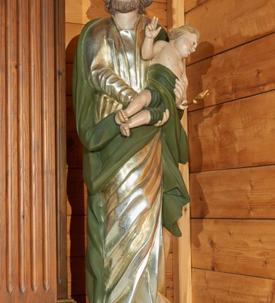 Zdjęcie nr 1: Rzeźba drążona, ustawiona na podstawie na planie prostokąta.  Święty ukazany frontalnie, z głową skierowana w prawo, obiema rękami podtrzymuje Dzieciątko Jezus. Twarz ma pociągłą, o migdałowatych, opadających oczach, prostym nosie i wąskich ustach; okoloną krótką brodą i jasnobrązowymi, kręconymi włosami sięgającymi ramion, z grzywką nad czołem.  Ubrany jest w srebrzoną tunikę silnie przylegającą do ciała, drapowaną w równoległe fałdy w partii torsu i ukośne w partii nóg. Na ramiona ma narzucony zielony płaszcz, zawinięty z przodu postaci. Jezus ukazany w pozycji półleżącej, zwrócony w trzech czwartych w lewo, prawą rękę unosi w geście błogosławieństwa, w lewej trzyma lilię. Twarz ma pociągłą, o migdałowatych oczach, zadarty nosie i wąskich ustach; okoloną krótkimi, jasnymi włosami. W partii podbrzusza owinięte jest zielonym płaszczem. Polichromia ciał figur naturalistyczna. 