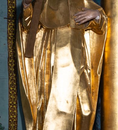 Zdjęcie nr 3: Rzeźba ścięta z tyłu, drążona, ustawiona na niskiej podstawie o ściętych narożach. Święty ukazany frontalnie, z głową skierowaną w lewo, w kontrapoście. W prawej, ugiętej i lekko uniesionej ręce trzyma krucyfiks, lewą dłoń kładzie na piersi. Twarz ma szczupłą, ascetyczną, o podkreślonej linii ściągniętych łuków brwiowych, głęboko osadzonych oczach z wyraźnie rytą górną powieką, skierowanych ku górze, dużym nosie i pełnych ustach z szeroką górną wargą. Twarz okolona krótką kręconą brodą oraz krótkimi falistymi puklami, na głowie tonsura. Ubrany jest w ściśle przylegający do ciała habit, przewiązany w talii, z lekko marszczonym szkaplerzem, na ramiona i plecy ma narzuconą pelerynkę z kapturem, z przodu krótką, a z tyłu sięgającą ziemi. Polichromia ciała naturalistyczna, szaty i atrybuty złocone.