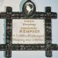 Zdjęcie nr 1: Płyta kamienna w formie leżącego prostokąta, ujęta drewnianą i polichromowaną ramą, o przecinających się listwach w narożach, dekorowaną płaskorzeźbionym ornamentem roślinnym. Zwieńczona owalnym, drewnianym medalionem z fotografią zmarłej na porcelanie. W polu płyty złocona inskrypcja: „PAMIĘCI / Stanisławy / z / GADOMSKICH / KEMPNER / + 7/3 1885 w 33 roku życia / Wdzięczny mąż z dziećmi.”