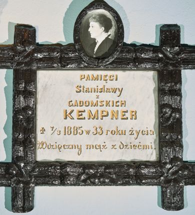 Zdjęcie nr 1: Płyta kamienna w formie leżącego prostokąta, ujęta drewnianą i polichromowaną ramą, o przecinających się listwach w narożach, dekorowaną płaskorzeźbionym ornamentem roślinnym. Zwieńczona owalnym, drewnianym medalionem z fotografią zmarłej na porcelanie. W polu płyty złocona inskrypcja: „PAMIĘCI / Stanisławy / z / GADOMSKICH / KEMPNER / + 7/3 1885 w 33 roku życia / Wdzięczny mąż z dziećmi.”