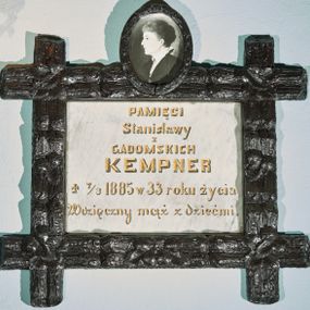 Zdjęcie nr 1: Płyta kamienna w formie leżącego prostokąta, ujęta drewnianą i polichromowaną ramą, o przecinających się listwach w narożach, dekorowaną płaskorzeźbionym ornamentem roślinnym. Zwieńczona owalnym, drewnianym medalionem z fotografią zmarłej na porcelanie. W polu płyty złocona inskrypcja: „PAMIĘCI / Stanisławy / z / GADOMSKICH / KEMPNER / + 7/3 1885 w 33 roku życia / Wdzięczny mąż z dziećmi.”