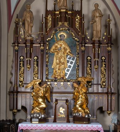 Zdjęcie nr 1: Nastawa architektoniczna, trójosiowa, jednokondygnacyjna ze zwieńczeniem, z predellą. Ołtarz prostopadłościenny, z drewnianą mensą i kamiennym portatylem. Antepedium ujęte grubą opaską, w polu płaskorzeźbiona otwarta księga z napisem „UBODZY / SKARBEM / KOŚCIOŁA” z liściem palmy i kratą. Na mensie tabernakulum w formie drewnianej skrzynki flankowanej pinaklami z kwiatonami. Drzwiczki w kształcie prostokąta zamkniętego łukiem ostrym, w ramie, z przedstawieniem baranka apokaliptycznego. Tabernakulum flankowane dwiema figurami klęczących na obłokach aniołów.  Osie nastawy wydzielone wąskimi kolumnami dźwigającymi stylizowane pinakle. W polu środkowym wnęka w formie stojącego prostokąta zamkniętego łukiem odcinkowym nadwieszonym, z obrazem św. Wawrzyńca, ujętym ramą zdobioną ornamentem roślinnym. W polach osi bocznych po dwie ażurowe stylizowane blendy wypełnione ornamentem roślinnym, pomiędzy nimi, w górnej partii, ośmioboczne wsporniki, na których stoją figury św. Izydora i św. Kryspina. Zwieńczenie w formie ośmiobocznego cokołu z figurą św. Józefa, flankowanego dwiema parami pinakli i blendami z dekoracja roślinną. Struktura pokryta politurą w kolorze ciemnobrązowym, ornamentyka i detale architektoniczne złocone. 
