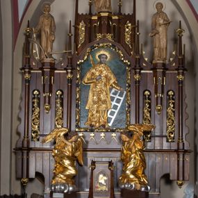 Zdjęcie nr 1: Nastawa architektoniczna, trójosiowa, jednokondygnacyjna ze zwieńczeniem, z predellą. Ołtarz prostopadłościenny, z drewnianą mensą i kamiennym portatylem. Antepedium ujęte grubą opaską, w polu płaskorzeźbiona otwarta księga z napisem „UBODZY / SKARBEM / KOŚCIOŁA” z liściem palmy i kratą. Na mensie tabernakulum w formie drewnianej skrzynki flankowanej pinaklami z kwiatonami. Drzwiczki w kształcie prostokąta zamkniętego łukiem ostrym, w ramie, z przedstawieniem baranka apokaliptycznego. Tabernakulum flankowane dwiema figurami klęczących na obłokach aniołów.  Osie nastawy wydzielone wąskimi kolumnami dźwigającymi stylizowane pinakle. W polu środkowym wnęka w formie stojącego prostokąta zamkniętego łukiem odcinkowym nadwieszonym, z obrazem św. Wawrzyńca, ujętym ramą zdobioną ornamentem roślinnym. W polach osi bocznych po dwie ażurowe stylizowane blendy wypełnione ornamentem roślinnym, pomiędzy nimi, w górnej partii, ośmioboczne wsporniki, na których stoją figury św. Izydora i św. Kryspina. Zwieńczenie w formie ośmiobocznego cokołu z figurą św. Józefa, flankowanego dwiema parami pinakli i blendami z dekoracja roślinną. Struktura pokryta politurą w kolorze ciemnobrązowym, ornamentyka i detale architektoniczne złocone. 
