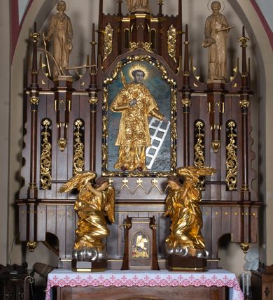 Zdjęcie nr 2: Nastawa architektoniczna, trójosiowa, jednokondygnacyjna ze zwieńczeniem, z predellą. Ołtarz prostopadłościenny, z drewnianą mensą i kamiennym portatylem. Antepedium ujęte grubą opaską, w polu płaskorzeźbiona otwarta księga z napisem „UBODZY / SKARBEM / KOŚCIOŁA” z liściem palmy i kratą. Na mensie tabernakulum w formie drewnianej skrzynki flankowanej pinaklami z kwiatonami. Drzwiczki w kształcie prostokąta zamkniętego łukiem ostrym, w ramie, z przedstawieniem baranka apokaliptycznego. Tabernakulum flankowane dwiema figurami klęczących na obłokach aniołów.  Osie nastawy wydzielone wąskimi kolumnami dźwigającymi stylizowane pinakle. W polu środkowym wnęka w formie stojącego prostokąta zamkniętego łukiem odcinkowym nadwieszonym, z obrazem św. Wawrzyńca, ujętym ramą zdobioną ornamentem roślinnym. W polach osi bocznych po dwie ażurowe stylizowane blendy wypełnione ornamentem roślinnym, pomiędzy nimi, w górnej partii, ośmioboczne wsporniki, na których stoją figury św. Izydora i św. Kryspina. Zwieńczenie w formie ośmiobocznego cokołu z figurą św. Józefa, flankowanego dwiema parami pinakli i blendami z dekoracja roślinną. Struktura pokryta politurą w kolorze ciemnobrązowym, ornamentyka i detale architektoniczne złocone. 
