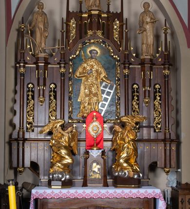 Zdjęcie nr 16: Nastawa architektoniczna, trójosiowa, jednokondygnacyjna ze zwieńczeniem, z predellą. Ołtarz prostopadłościenny, z drewnianą mensą i kamiennym portatylem. Antepedium ujęte grubą opaską, w polu płaskorzeźbiona otwarta księga z napisem „UBODZY / SKARBEM / KOŚCIOŁA” z liściem palmy i kratą. Na mensie tabernakulum w formie drewnianej skrzynki flankowanej pinaklami z kwiatonami. Drzwiczki w kształcie prostokąta zamkniętego łukiem ostrym, w ramie, z przedstawieniem baranka apokaliptycznego. Tabernakulum flankowane dwiema figurami klęczących na obłokach aniołów.  Osie nastawy wydzielone wąskimi kolumnami dźwigającymi stylizowane pinakle. W polu środkowym wnęka w formie stojącego prostokąta zamkniętego łukiem odcinkowym nadwieszonym, z obrazem św. Wawrzyńca, ujętym ramą zdobioną ornamentem roślinnym. W polach osi bocznych po dwie ażurowe stylizowane blendy wypełnione ornamentem roślinnym, pomiędzy nimi, w górnej partii, ośmioboczne wsporniki, na których stoją figury św. Izydora i św. Kryspina. Zwieńczenie w formie ośmiobocznego cokołu z figurą św. Józefa, flankowanego dwiema parami pinakli i blendami z dekoracja roślinną. Struktura pokryta politurą w kolorze ciemnobrązowym, ornamentyka i detale architektoniczne złocone. 
