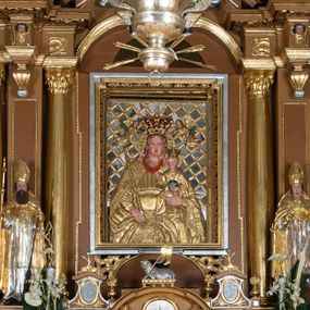 Zdjęcie nr 1: Nastawa ołtarzowa architektoniczna, jednoosiowa, jednokondygnacyjna z bramkami i zwieńczeniem, ustawiona na wysokim, dwustrefowym cokole. Ołtarz prostopadłościenny, murowany, umieszczony w drewnianej obudowie. Antependium ujęte ramą dekorowaną plecionką, podzielone na trzy pola: w środkowym płaskorzeźbione przedstawienie Ostatniej Wieczerzy według Leonarda da Vinci, a po bokach ornament roślinny o wertykalnym układzie.

Tabernakulum architektoniczne, jednokondygnacyjne, trójosiowe, ustawione na zdwojonym na cokole z dwoma zwieńczeniami na osiach skrajnych. Osie wydzielone są parami kolumn o kapitelach kompozytowych, oś środkowa wysunięta do przodu. Podpory dźwigają pełne belkowanie wyłamane na ich linii, przerwane nad polem środkowym, gdzie kolumny dźwigają przerwany półkolisty przyczółek połączony z łukiem gzymsu, nad nim ustawiona jest rzeźba Baranka leżącego na księdze z siedmioma pieczęciami. W polu środkowym dwuskrzydłowe drzwiczki do metalowego tabernakulum ujęte ramą w formie stojącego prostokąta, zamkniętego łukiem nadwieszonym z długim uskokiem. Na drzwiczkach znajdują się dwa aplikowane klęczące anioły, powyżej Chrismo w medalionie, otoczonym glorią. W osiach bocznych są nisze zamknięte konchami z figurkami aniołów, zamknięte zwieńczeniami w formie stojących prostokątów z falistym gzymsem i gałązkami lilii na szczycie; w polu srebrzone, owalne medaliony. Po bokach kondygnacji na wolutowych uszach oraz po bokach zwieńczeń znajdują się wazony ze słonecznikami. Cokół zdobiony jest ornamentem akantowym.

Kondygnacja ujęta jest dwiema parami kolumn o kapitelach kompozytowych oraz stojącą między nimi parą filarów. Podpory dźwigają pełne belkowanie o silnie wysuniętym gzymsie, wyłamane na osiach bocznych, z podwieszonymi szyszkami na tle filarów; przerwane nad polem środkowym. W centrum pole w formie stojącego prostokąta ujęte ramą dekorowaną ornamentem roślinnym z płaskorzeźbionym przedstawieniem Matki Boskiej z Dzieciątkiem. Na zasuwie obrazy: „Najświętsze Serce Pana Jezusa”, „Zwiastowanie” oraz „Św. Mikołaj”. Nad bramkami oraz pomiędzy kolumnami ustawione są rzeźby. Od lewej kolejno: św. Andrzej, św. Wojciech, św. Stanisław i na końcu po prawej św. Tomasz. Nad polem głównym znajduje się przeszklony prześwit w formie półkola z rzeźbioną gołębicą Ducha Świętego na tle glorii. Powyżej pole zamknięte półkoliście fragmentem gzymsu z rzeźbionym popiersiem błogosławiącego Boga Ojca pośród obłoków. Zwieńczenie w formie zbliżonej do stojącego prostokąta o wklęsłych bokach z gzymsem i z podwieszonym lambrekinem oraz kotarami spływającymi na boki. W polu przeszklony prześwit w formie kwadratu zamkniętego łukiem nadwieszonym z rzeźbionym monogramem Marii na tle glorii. Po bokach zwieńczenia ustawione są dwie duże figury klęczących aniołów.

Bramki po bokach ołtarza ustawione są na wysokości cokołu nastawy; przejścia ujęte są parą kanelowanych pilastrów, zamknięte łukiem utworzonym z dwóch przeciwstawnych wolut wspierających wieńczące cokoły. Przejścia w formie wydłużonego stojącego prostokąta zamkniętego łukiem półkolistym nadwieszonym.

Całość ołtarza oprócz tabernakulum dekorowana jest ornamentem małżowinowo-chrząstkowym. Uszy flankujące kondygnację utworzone są również z ornamentu małżowinowo-chrząstkowego. Na zamknięciu zwieńczenia znajdują się dwie uskrzydlone główki anielskie skierowane na wprost z podwieszonymi u szyi chustami. Struktura ołtarza polichromowana jest w kolorze brązowym ze złoconymi kolumnami, ornamentyką i profilami, detale srebrzone.