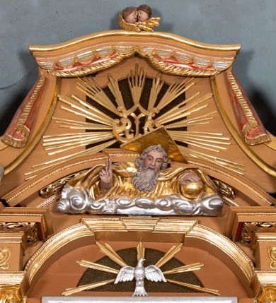 Zdjęcie nr 6: Nastawa ołtarzowa architektoniczna, jednoosiowa, jednokondygnacyjna z bramkami i zwieńczeniem, ustawiona na wysokim, dwustrefowym cokole. Ołtarz prostopadłościenny, murowany, umieszczony w drewnianej obudowie. Antependium ujęte ramą dekorowaną plecionką, podzielone na trzy pola: w środkowym płaskorzeźbione przedstawienie Ostatniej Wieczerzy według Leonarda da Vinci, a po bokach ornament roślinny o wertykalnym układzie.

Tabernakulum architektoniczne, jednokondygnacyjne, trójosiowe, ustawione na zdwojonym na cokole z dwoma zwieńczeniami na osiach skrajnych. Osie wydzielone są parami kolumn o kapitelach kompozytowych, oś środkowa wysunięta do przodu. Podpory dźwigają pełne belkowanie wyłamane na ich linii, przerwane nad polem środkowym, gdzie kolumny dźwigają przerwany półkolisty przyczółek połączony z łukiem gzymsu, nad nim ustawiona jest rzeźba Baranka leżącego na księdze z siedmioma pieczęciami. W polu środkowym dwuskrzydłowe drzwiczki do metalowego tabernakulum ujęte ramą w formie stojącego prostokąta, zamkniętego łukiem nadwieszonym z długim uskokiem. Na drzwiczkach znajdują się dwa aplikowane klęczące anioły, powyżej Chrismo w medalionie, otoczonym glorią. W osiach bocznych są nisze zamknięte konchami z figurkami aniołów, zamknięte zwieńczeniami w formie stojących prostokątów z falistym gzymsem i gałązkami lilii na szczycie; w polu srebrzone, owalne medaliony. Po bokach kondygnacji na wolutowych uszach oraz po bokach zwieńczeń znajdują się wazony ze słonecznikami. Cokół zdobiony jest ornamentem akantowym.

Kondygnacja ujęta jest dwiema parami kolumn o kapitelach kompozytowych oraz stojącą między nimi parą filarów. Podpory dźwigają pełne belkowanie o silnie wysuniętym gzymsie, wyłamane na osiach bocznych, z podwieszonymi szyszkami na tle filarów; przerwane nad polem środkowym. W centrum pole w formie stojącego prostokąta ujęte ramą dekorowaną ornamentem roślinnym z płaskorzeźbionym przedstawieniem Matki Boskiej z Dzieciątkiem. Na zasuwie obrazy: „Najświętsze Serce Pana Jezusa”, „Zwiastowanie” oraz „Św. Mikołaj”. Nad bramkami oraz pomiędzy kolumnami ustawione są rzeźby. Od lewej kolejno: św. Andrzej, św. Wojciech, św. Stanisław i na końcu po prawej św. Tomasz. Nad polem głównym znajduje się przeszklony prześwit w formie półkola z rzeźbioną gołębicą Ducha Świętego na tle glorii. Powyżej pole zamknięte półkoliście fragmentem gzymsu z rzeźbionym popiersiem błogosławiącego Boga Ojca pośród obłoków. Zwieńczenie w formie zbliżonej do stojącego prostokąta o wklęsłych bokach z gzymsem i z podwieszonym lambrekinem oraz kotarami spływającymi na boki. W polu przeszklony prześwit w formie kwadratu zamkniętego łukiem nadwieszonym z rzeźbionym monogramem Marii na tle glorii. Po bokach zwieńczenia ustawione są dwie duże figury klęczących aniołów.

Bramki po bokach ołtarza ustawione są na wysokości cokołu nastawy; przejścia ujęte są parą kanelowanych pilastrów, zamknięte łukiem utworzonym z dwóch przeciwstawnych wolut wspierających wieńczące cokoły. Przejścia w formie wydłużonego stojącego prostokąta zamkniętego łukiem półkolistym nadwieszonym.

Całość ołtarza oprócz tabernakulum dekorowana jest ornamentem małżowinowo-chrząstkowym. Uszy flankujące kondygnację utworzone są również z ornamentu małżowinowo-chrząstkowego. Na zamknięciu zwieńczenia znajdują się dwie uskrzydlone główki anielskie skierowane na wprost z podwieszonymi u szyi chustami. Struktura ołtarza polichromowana jest w kolorze brązowym ze złoconymi kolumnami, ornamentyką i profilami, detale srebrzone.