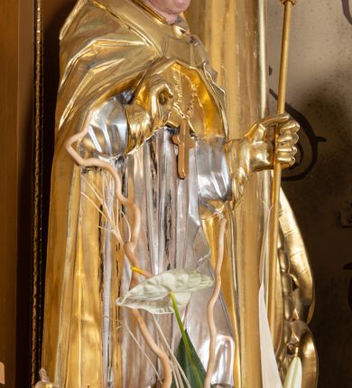 Zdjęcie nr 15: Nastawa ołtarzowa architektoniczna, jednoosiowa, jednokondygnacyjna z bramkami i zwieńczeniem, ustawiona na wysokim, dwustrefowym cokole. Ołtarz prostopadłościenny, murowany, umieszczony w drewnianej obudowie. Antependium ujęte ramą dekorowaną plecionką, podzielone na trzy pola: w środkowym płaskorzeźbione przedstawienie Ostatniej Wieczerzy według Leonarda da Vinci, a po bokach ornament roślinny o wertykalnym układzie.

Tabernakulum architektoniczne, jednokondygnacyjne, trójosiowe, ustawione na zdwojonym na cokole z dwoma zwieńczeniami na osiach skrajnych. Osie wydzielone są parami kolumn o kapitelach kompozytowych, oś środkowa wysunięta do przodu. Podpory dźwigają pełne belkowanie wyłamane na ich linii, przerwane nad polem środkowym, gdzie kolumny dźwigają przerwany półkolisty przyczółek połączony z łukiem gzymsu, nad nim ustawiona jest rzeźba Baranka leżącego na księdze z siedmioma pieczęciami. W polu środkowym dwuskrzydłowe drzwiczki do metalowego tabernakulum ujęte ramą w formie stojącego prostokąta, zamkniętego łukiem nadwieszonym z długim uskokiem. Na drzwiczkach znajdują się dwa aplikowane klęczące anioły, powyżej Chrismo w medalionie, otoczonym glorią. W osiach bocznych są nisze zamknięte konchami z figurkami aniołów, zamknięte zwieńczeniami w formie stojących prostokątów z falistym gzymsem i gałązkami lilii na szczycie; w polu srebrzone, owalne medaliony. Po bokach kondygnacji na wolutowych uszach oraz po bokach zwieńczeń znajdują się wazony ze słonecznikami. Cokół zdobiony jest ornamentem akantowym.

Kondygnacja ujęta jest dwiema parami kolumn o kapitelach kompozytowych oraz stojącą między nimi parą filarów. Podpory dźwigają pełne belkowanie o silnie wysuniętym gzymsie, wyłamane na osiach bocznych, z podwieszonymi szyszkami na tle filarów; przerwane nad polem środkowym. W centrum pole w formie stojącego prostokąta ujęte ramą dekorowaną ornamentem roślinnym z płaskorzeźbionym przedstawieniem Matki Boskiej z Dzieciątkiem. Na zasuwie obrazy: „Najświętsze Serce Pana Jezusa”, „Zwiastowanie” oraz „Św. Mikołaj”. Nad bramkami oraz pomiędzy kolumnami ustawione są rzeźby. Od lewej kolejno: św. Andrzej, św. Wojciech, św. Stanisław i na końcu po prawej św. Tomasz. Nad polem głównym znajduje się przeszklony prześwit w formie półkola z rzeźbioną gołębicą Ducha Świętego na tle glorii. Powyżej pole zamknięte półkoliście fragmentem gzymsu z rzeźbionym popiersiem błogosławiącego Boga Ojca pośród obłoków. Zwieńczenie w formie zbliżonej do stojącego prostokąta o wklęsłych bokach z gzymsem i z podwieszonym lambrekinem oraz kotarami spływającymi na boki. W polu przeszklony prześwit w formie kwadratu zamkniętego łukiem nadwieszonym z rzeźbionym monogramem Marii na tle glorii. Po bokach zwieńczenia ustawione są dwie duże figury klęczących aniołów.

Bramki po bokach ołtarza ustawione są na wysokości cokołu nastawy; przejścia ujęte są parą kanelowanych pilastrów, zamknięte łukiem utworzonym z dwóch przeciwstawnych wolut wspierających wieńczące cokoły. Przejścia w formie wydłużonego stojącego prostokąta zamkniętego łukiem półkolistym nadwieszonym.

Całość ołtarza oprócz tabernakulum dekorowana jest ornamentem małżowinowo-chrząstkowym. Uszy flankujące kondygnację utworzone są również z ornamentu małżowinowo-chrząstkowego. Na zamknięciu zwieńczenia znajdują się dwie uskrzydlone główki anielskie skierowane na wprost z podwieszonymi u szyi chustami. Struktura ołtarza polichromowana jest w kolorze brązowym ze złoconymi kolumnami, ornamentyką i profilami, detale srebrzone.