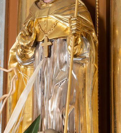 Zdjęcie nr 16: Nastawa ołtarzowa architektoniczna, jednoosiowa, jednokondygnacyjna z bramkami i zwieńczeniem, ustawiona na wysokim, dwustrefowym cokole. Ołtarz prostopadłościenny, murowany, umieszczony w drewnianej obudowie. Antependium ujęte ramą dekorowaną plecionką, podzielone na trzy pola: w środkowym płaskorzeźbione przedstawienie Ostatniej Wieczerzy według Leonarda da Vinci, a po bokach ornament roślinny o wertykalnym układzie.

Tabernakulum architektoniczne, jednokondygnacyjne, trójosiowe, ustawione na zdwojonym na cokole z dwoma zwieńczeniami na osiach skrajnych. Osie wydzielone są parami kolumn o kapitelach kompozytowych, oś środkowa wysunięta do przodu. Podpory dźwigają pełne belkowanie wyłamane na ich linii, przerwane nad polem środkowym, gdzie kolumny dźwigają przerwany półkolisty przyczółek połączony z łukiem gzymsu, nad nim ustawiona jest rzeźba Baranka leżącego na księdze z siedmioma pieczęciami. W polu środkowym dwuskrzydłowe drzwiczki do metalowego tabernakulum ujęte ramą w formie stojącego prostokąta, zamkniętego łukiem nadwieszonym z długim uskokiem. Na drzwiczkach znajdują się dwa aplikowane klęczące anioły, powyżej Chrismo w medalionie, otoczonym glorią. W osiach bocznych są nisze zamknięte konchami z figurkami aniołów, zamknięte zwieńczeniami w formie stojących prostokątów z falistym gzymsem i gałązkami lilii na szczycie; w polu srebrzone, owalne medaliony. Po bokach kondygnacji na wolutowych uszach oraz po bokach zwieńczeń znajdują się wazony ze słonecznikami. Cokół zdobiony jest ornamentem akantowym.

Kondygnacja ujęta jest dwiema parami kolumn o kapitelach kompozytowych oraz stojącą między nimi parą filarów. Podpory dźwigają pełne belkowanie o silnie wysuniętym gzymsie, wyłamane na osiach bocznych, z podwieszonymi szyszkami na tle filarów; przerwane nad polem środkowym. W centrum pole w formie stojącego prostokąta ujęte ramą dekorowaną ornamentem roślinnym z płaskorzeźbionym przedstawieniem Matki Boskiej z Dzieciątkiem. Na zasuwie obrazy: „Najświętsze Serce Pana Jezusa”, „Zwiastowanie” oraz „Św. Mikołaj”. Nad bramkami oraz pomiędzy kolumnami ustawione są rzeźby. Od lewej kolejno: św. Andrzej, św. Wojciech, św. Stanisław i na końcu po prawej św. Tomasz. Nad polem głównym znajduje się przeszklony prześwit w formie półkola z rzeźbioną gołębicą Ducha Świętego na tle glorii. Powyżej pole zamknięte półkoliście fragmentem gzymsu z rzeźbionym popiersiem błogosławiącego Boga Ojca pośród obłoków. Zwieńczenie w formie zbliżonej do stojącego prostokąta o wklęsłych bokach z gzymsem i z podwieszonym lambrekinem oraz kotarami spływającymi na boki. W polu przeszklony prześwit w formie kwadratu zamkniętego łukiem nadwieszonym z rzeźbionym monogramem Marii na tle glorii. Po bokach zwieńczenia ustawione są dwie duże figury klęczących aniołów.

Bramki po bokach ołtarza ustawione są na wysokości cokołu nastawy; przejścia ujęte są parą kanelowanych pilastrów, zamknięte łukiem utworzonym z dwóch przeciwstawnych wolut wspierających wieńczące cokoły. Przejścia w formie wydłużonego stojącego prostokąta zamkniętego łukiem półkolistym nadwieszonym.

Całość ołtarza oprócz tabernakulum dekorowana jest ornamentem małżowinowo-chrząstkowym. Uszy flankujące kondygnację utworzone są również z ornamentu małżowinowo-chrząstkowego. Na zamknięciu zwieńczenia znajdują się dwie uskrzydlone główki anielskie skierowane na wprost z podwieszonymi u szyi chustami. Struktura ołtarza polichromowana jest w kolorze brązowym ze złoconymi kolumnami, ornamentyką i profilami, detale srebrzone.