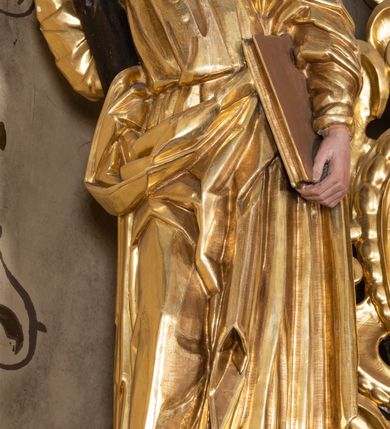 Zdjęcie nr 22: Nastawa ołtarzowa architektoniczna, jednoosiowa, jednokondygnacyjna z bramkami i zwieńczeniem, ustawiona na wysokim, dwustrefowym cokole. Ołtarz prostopadłościenny, murowany, umieszczony w drewnianej obudowie. Antependium ujęte ramą dekorowaną plecionką, podzielone na trzy pola: w środkowym płaskorzeźbione przedstawienie Ostatniej Wieczerzy według Leonarda da Vinci, a po bokach ornament roślinny o wertykalnym układzie.

Tabernakulum architektoniczne, jednokondygnacyjne, trójosiowe, ustawione na zdwojonym na cokole z dwoma zwieńczeniami na osiach skrajnych. Osie wydzielone są parami kolumn o kapitelach kompozytowych, oś środkowa wysunięta do przodu. Podpory dźwigają pełne belkowanie wyłamane na ich linii, przerwane nad polem środkowym, gdzie kolumny dźwigają przerwany półkolisty przyczółek połączony z łukiem gzymsu, nad nim ustawiona jest rzeźba Baranka leżącego na księdze z siedmioma pieczęciami. W polu środkowym dwuskrzydłowe drzwiczki do metalowego tabernakulum ujęte ramą w formie stojącego prostokąta, zamkniętego łukiem nadwieszonym z długim uskokiem. Na drzwiczkach znajdują się dwa aplikowane klęczące anioły, powyżej Chrismo w medalionie, otoczonym glorią. W osiach bocznych są nisze zamknięte konchami z figurkami aniołów, zamknięte zwieńczeniami w formie stojących prostokątów z falistym gzymsem i gałązkami lilii na szczycie; w polu srebrzone, owalne medaliony. Po bokach kondygnacji na wolutowych uszach oraz po bokach zwieńczeń znajdują się wazony ze słonecznikami. Cokół zdobiony jest ornamentem akantowym.

Kondygnacja ujęta jest dwiema parami kolumn o kapitelach kompozytowych oraz stojącą między nimi parą filarów. Podpory dźwigają pełne belkowanie o silnie wysuniętym gzymsie, wyłamane na osiach bocznych, z podwieszonymi szyszkami na tle filarów; przerwane nad polem środkowym. W centrum pole w formie stojącego prostokąta ujęte ramą dekorowaną ornamentem roślinnym z płaskorzeźbionym przedstawieniem Matki Boskiej z Dzieciątkiem. Na zasuwie obrazy: „Najświętsze Serce Pana Jezusa”, „Zwiastowanie” oraz „Św. Mikołaj”. Nad bramkami oraz pomiędzy kolumnami ustawione są rzeźby. Od lewej kolejno: św. Andrzej, św. Wojciech, św. Stanisław i na końcu po prawej św. Tomasz. Nad polem głównym znajduje się przeszklony prześwit w formie półkola z rzeźbioną gołębicą Ducha Świętego na tle glorii. Powyżej pole zamknięte półkoliście fragmentem gzymsu z rzeźbionym popiersiem błogosławiącego Boga Ojca pośród obłoków. Zwieńczenie w formie zbliżonej do stojącego prostokąta o wklęsłych bokach z gzymsem i z podwieszonym lambrekinem oraz kotarami spływającymi na boki. W polu przeszklony prześwit w formie kwadratu zamkniętego łukiem nadwieszonym z rzeźbionym monogramem Marii na tle glorii. Po bokach zwieńczenia ustawione są dwie duże figury klęczących aniołów.

Bramki po bokach ołtarza ustawione są na wysokości cokołu nastawy; przejścia ujęte są parą kanelowanych pilastrów, zamknięte łukiem utworzonym z dwóch przeciwstawnych wolut wspierających wieńczące cokoły. Przejścia w formie wydłużonego stojącego prostokąta zamkniętego łukiem półkolistym nadwieszonym.

Całość ołtarza oprócz tabernakulum dekorowana jest ornamentem małżowinowo-chrząstkowym. Uszy flankujące kondygnację utworzone są również z ornamentu małżowinowo-chrząstkowego. Na zamknięciu zwieńczenia znajdują się dwie uskrzydlone główki anielskie skierowane na wprost z podwieszonymi u szyi chustami. Struktura ołtarza polichromowana jest w kolorze brązowym ze złoconymi kolumnami, ornamentyką i profilami, detale srebrzone.