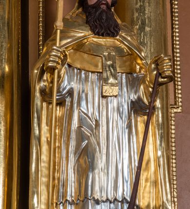 Zdjęcie nr 27: Nastawa ołtarzowa architektoniczna, jednoosiowa, jednokondygnacyjna z bramkami i zwieńczeniem, ustawiona na wysokim, dwustrefowym cokole. Ołtarz prostopadłościenny, murowany, umieszczony w drewnianej obudowie. Antependium ujęte ramą dekorowaną plecionką, podzielone na trzy pola: w środkowym płaskorzeźbione przedstawienie Ostatniej Wieczerzy według Leonarda da Vinci, a po bokach ornament roślinny o wertykalnym układzie.

Tabernakulum architektoniczne, jednokondygnacyjne, trójosiowe, ustawione na zdwojonym na cokole z dwoma zwieńczeniami na osiach skrajnych. Osie wydzielone są parami kolumn o kapitelach kompozytowych, oś środkowa wysunięta do przodu. Podpory dźwigają pełne belkowanie wyłamane na ich linii, przerwane nad polem środkowym, gdzie kolumny dźwigają przerwany półkolisty przyczółek połączony z łukiem gzymsu, nad nim ustawiona jest rzeźba Baranka leżącego na księdze z siedmioma pieczęciami. W polu środkowym dwuskrzydłowe drzwiczki do metalowego tabernakulum ujęte ramą w formie stojącego prostokąta, zamkniętego łukiem nadwieszonym z długim uskokiem. Na drzwiczkach znajdują się dwa aplikowane klęczące anioły, powyżej Chrismo w medalionie, otoczonym glorią. W osiach bocznych są nisze zamknięte konchami z figurkami aniołów, zamknięte zwieńczeniami w formie stojących prostokątów z falistym gzymsem i gałązkami lilii na szczycie; w polu srebrzone, owalne medaliony. Po bokach kondygnacji na wolutowych uszach oraz po bokach zwieńczeń znajdują się wazony ze słonecznikami. Cokół zdobiony jest ornamentem akantowym.

Kondygnacja ujęta jest dwiema parami kolumn o kapitelach kompozytowych oraz stojącą między nimi parą filarów. Podpory dźwigają pełne belkowanie o silnie wysuniętym gzymsie, wyłamane na osiach bocznych, z podwieszonymi szyszkami na tle filarów; przerwane nad polem środkowym. W centrum pole w formie stojącego prostokąta ujęte ramą dekorowaną ornamentem roślinnym z płaskorzeźbionym przedstawieniem Matki Boskiej z Dzieciątkiem. Na zasuwie obrazy: „Najświętsze Serce Pana Jezusa”, „Zwiastowanie” oraz „Św. Mikołaj”. Nad bramkami oraz pomiędzy kolumnami ustawione są rzeźby. Od lewej kolejno: św. Andrzej, św. Wojciech, św. Stanisław i na końcu po prawej św. Tomasz. Nad polem głównym znajduje się przeszklony prześwit w formie półkola z rzeźbioną gołębicą Ducha Świętego na tle glorii. Powyżej pole zamknięte półkoliście fragmentem gzymsu z rzeźbionym popiersiem błogosławiącego Boga Ojca pośród obłoków. Zwieńczenie w formie zbliżonej do stojącego prostokąta o wklęsłych bokach z gzymsem i z podwieszonym lambrekinem oraz kotarami spływającymi na boki. W polu przeszklony prześwit w formie kwadratu zamkniętego łukiem nadwieszonym z rzeźbionym monogramem Marii na tle glorii. Po bokach zwieńczenia ustawione są dwie duże figury klęczących aniołów.

Bramki po bokach ołtarza ustawione są na wysokości cokołu nastawy; przejścia ujęte są parą kanelowanych pilastrów, zamknięte łukiem utworzonym z dwóch przeciwstawnych wolut wspierających wieńczące cokoły. Przejścia w formie wydłużonego stojącego prostokąta zamkniętego łukiem półkolistym nadwieszonym.

Całość ołtarza oprócz tabernakulum dekorowana jest ornamentem małżowinowo-chrząstkowym. Uszy flankujące kondygnację utworzone są również z ornamentu małżowinowo-chrząstkowego. Na zamknięciu zwieńczenia znajdują się dwie uskrzydlone główki anielskie skierowane na wprost z podwieszonymi u szyi chustami. Struktura ołtarza polichromowana jest w kolorze brązowym ze złoconymi kolumnami, ornamentyką i profilami, detale srebrzone.