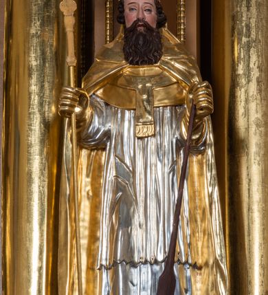 Zdjęcie nr 28: Nastawa ołtarzowa architektoniczna, jednoosiowa, jednokondygnacyjna z bramkami i zwieńczeniem, ustawiona na wysokim, dwustrefowym cokole. Ołtarz prostopadłościenny, murowany, umieszczony w drewnianej obudowie. Antependium ujęte ramą dekorowaną plecionką, podzielone na trzy pola: w środkowym płaskorzeźbione przedstawienie Ostatniej Wieczerzy według Leonarda da Vinci, a po bokach ornament roślinny o wertykalnym układzie.

Tabernakulum architektoniczne, jednokondygnacyjne, trójosiowe, ustawione na zdwojonym na cokole z dwoma zwieńczeniami na osiach skrajnych. Osie wydzielone są parami kolumn o kapitelach kompozytowych, oś środkowa wysunięta do przodu. Podpory dźwigają pełne belkowanie wyłamane na ich linii, przerwane nad polem środkowym, gdzie kolumny dźwigają przerwany półkolisty przyczółek połączony z łukiem gzymsu, nad nim ustawiona jest rzeźba Baranka leżącego na księdze z siedmioma pieczęciami. W polu środkowym dwuskrzydłowe drzwiczki do metalowego tabernakulum ujęte ramą w formie stojącego prostokąta, zamkniętego łukiem nadwieszonym z długim uskokiem. Na drzwiczkach znajdują się dwa aplikowane klęczące anioły, powyżej Chrismo w medalionie, otoczonym glorią. W osiach bocznych są nisze zamknięte konchami z figurkami aniołów, zamknięte zwieńczeniami w formie stojących prostokątów z falistym gzymsem i gałązkami lilii na szczycie; w polu srebrzone, owalne medaliony. Po bokach kondygnacji na wolutowych uszach oraz po bokach zwieńczeń znajdują się wazony ze słonecznikami. Cokół zdobiony jest ornamentem akantowym.

Kondygnacja ujęta jest dwiema parami kolumn o kapitelach kompozytowych oraz stojącą między nimi parą filarów. Podpory dźwigają pełne belkowanie o silnie wysuniętym gzymsie, wyłamane na osiach bocznych, z podwieszonymi szyszkami na tle filarów; przerwane nad polem środkowym. W centrum pole w formie stojącego prostokąta ujęte ramą dekorowaną ornamentem roślinnym z płaskorzeźbionym przedstawieniem Matki Boskiej z Dzieciątkiem. Na zasuwie obrazy: „Najświętsze Serce Pana Jezusa”, „Zwiastowanie” oraz „Św. Mikołaj”. Nad bramkami oraz pomiędzy kolumnami ustawione są rzeźby. Od lewej kolejno: św. Andrzej, św. Wojciech, św. Stanisław i na końcu po prawej św. Tomasz. Nad polem głównym znajduje się przeszklony prześwit w formie półkola z rzeźbioną gołębicą Ducha Świętego na tle glorii. Powyżej pole zamknięte półkoliście fragmentem gzymsu z rzeźbionym popiersiem błogosławiącego Boga Ojca pośród obłoków. Zwieńczenie w formie zbliżonej do stojącego prostokąta o wklęsłych bokach z gzymsem i z podwieszonym lambrekinem oraz kotarami spływającymi na boki. W polu przeszklony prześwit w formie kwadratu zamkniętego łukiem nadwieszonym z rzeźbionym monogramem Marii na tle glorii. Po bokach zwieńczenia ustawione są dwie duże figury klęczących aniołów.

Bramki po bokach ołtarza ustawione są na wysokości cokołu nastawy; przejścia ujęte są parą kanelowanych pilastrów, zamknięte łukiem utworzonym z dwóch przeciwstawnych wolut wspierających wieńczące cokoły. Przejścia w formie wydłużonego stojącego prostokąta zamkniętego łukiem półkolistym nadwieszonym.

Całość ołtarza oprócz tabernakulum dekorowana jest ornamentem małżowinowo-chrząstkowym. Uszy flankujące kondygnację utworzone są również z ornamentu małżowinowo-chrząstkowego. Na zamknięciu zwieńczenia znajdują się dwie uskrzydlone główki anielskie skierowane na wprost z podwieszonymi u szyi chustami. Struktura ołtarza polichromowana jest w kolorze brązowym ze złoconymi kolumnami, ornamentyką i profilami, detale srebrzone.