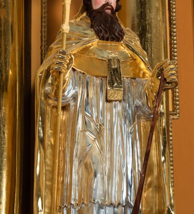 Zdjęcie nr 54: Nastawa ołtarzowa architektoniczna, jednoosiowa, jednokondygnacyjna z bramkami i zwieńczeniem, ustawiona na wysokim, dwustrefowym cokole. Ołtarz prostopadłościenny, murowany, umieszczony w drewnianej obudowie. Antependium ujęte ramą dekorowaną plecionką, podzielone na trzy pola: w środkowym płaskorzeźbione przedstawienie Ostatniej Wieczerzy według Leonarda da Vinci, a po bokach ornament roślinny o wertykalnym układzie.

Tabernakulum architektoniczne, jednokondygnacyjne, trójosiowe, ustawione na zdwojonym na cokole z dwoma zwieńczeniami na osiach skrajnych. Osie wydzielone są parami kolumn o kapitelach kompozytowych, oś środkowa wysunięta do przodu. Podpory dźwigają pełne belkowanie wyłamane na ich linii, przerwane nad polem środkowym, gdzie kolumny dźwigają przerwany półkolisty przyczółek połączony z łukiem gzymsu, nad nim ustawiona jest rzeźba Baranka leżącego na księdze z siedmioma pieczęciami. W polu środkowym dwuskrzydłowe drzwiczki do metalowego tabernakulum ujęte ramą w formie stojącego prostokąta, zamkniętego łukiem nadwieszonym z długim uskokiem. Na drzwiczkach znajdują się dwa aplikowane klęczące anioły, powyżej Chrismo w medalionie, otoczonym glorią. W osiach bocznych są nisze zamknięte konchami z figurkami aniołów, zamknięte zwieńczeniami w formie stojących prostokątów z falistym gzymsem i gałązkami lilii na szczycie; w polu srebrzone, owalne medaliony. Po bokach kondygnacji na wolutowych uszach oraz po bokach zwieńczeń znajdują się wazony ze słonecznikami. Cokół zdobiony jest ornamentem akantowym.

Kondygnacja ujęta jest dwiema parami kolumn o kapitelach kompozytowych oraz stojącą między nimi parą filarów. Podpory dźwigają pełne belkowanie o silnie wysuniętym gzymsie, wyłamane na osiach bocznych, z podwieszonymi szyszkami na tle filarów; przerwane nad polem środkowym. W centrum pole w formie stojącego prostokąta ujęte ramą dekorowaną ornamentem roślinnym z płaskorzeźbionym przedstawieniem Matki Boskiej z Dzieciątkiem. Na zasuwie obrazy: „Najświętsze Serce Pana Jezusa”, „Zwiastowanie” oraz „Św. Mikołaj”. Nad bramkami oraz pomiędzy kolumnami ustawione są rzeźby. Od lewej kolejno: św. Andrzej, św. Wojciech, św. Stanisław i na końcu po prawej św. Tomasz. Nad polem głównym znajduje się przeszklony prześwit w formie półkola z rzeźbioną gołębicą Ducha Świętego na tle glorii. Powyżej pole zamknięte półkoliście fragmentem gzymsu z rzeźbionym popiersiem błogosławiącego Boga Ojca pośród obłoków. Zwieńczenie w formie zbliżonej do stojącego prostokąta o wklęsłych bokach z gzymsem i z podwieszonym lambrekinem oraz kotarami spływającymi na boki. W polu przeszklony prześwit w formie kwadratu zamkniętego łukiem nadwieszonym z rzeźbionym monogramem Marii na tle glorii. Po bokach zwieńczenia ustawione są dwie duże figury klęczących aniołów.

Bramki po bokach ołtarza ustawione są na wysokości cokołu nastawy; przejścia ujęte są parą kanelowanych pilastrów, zamknięte łukiem utworzonym z dwóch przeciwstawnych wolut wspierających wieńczące cokoły. Przejścia w formie wydłużonego stojącego prostokąta zamkniętego łukiem półkolistym nadwieszonym.

Całość ołtarza oprócz tabernakulum dekorowana jest ornamentem małżowinowo-chrząstkowym. Uszy flankujące kondygnację utworzone są również z ornamentu małżowinowo-chrząstkowego. Na zamknięciu zwieńczenia znajdują się dwie uskrzydlone główki anielskie skierowane na wprost z podwieszonymi u szyi chustami. Struktura ołtarza polichromowana jest w kolorze brązowym ze złoconymi kolumnami, ornamentyką i profilami, detale srebrzone.