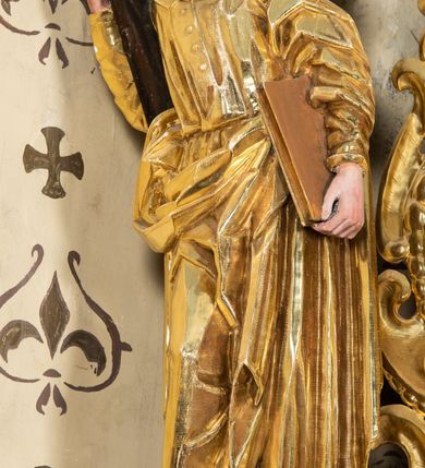 Zdjęcie nr 56: Nastawa ołtarzowa architektoniczna, jednoosiowa, jednokondygnacyjna z bramkami i zwieńczeniem, ustawiona na wysokim, dwustrefowym cokole. Ołtarz prostopadłościenny, murowany, umieszczony w drewnianej obudowie. Antependium ujęte ramą dekorowaną plecionką, podzielone na trzy pola: w środkowym płaskorzeźbione przedstawienie Ostatniej Wieczerzy według Leonarda da Vinci, a po bokach ornament roślinny o wertykalnym układzie.

Tabernakulum architektoniczne, jednokondygnacyjne, trójosiowe, ustawione na zdwojonym na cokole z dwoma zwieńczeniami na osiach skrajnych. Osie wydzielone są parami kolumn o kapitelach kompozytowych, oś środkowa wysunięta do przodu. Podpory dźwigają pełne belkowanie wyłamane na ich linii, przerwane nad polem środkowym, gdzie kolumny dźwigają przerwany półkolisty przyczółek połączony z łukiem gzymsu, nad nim ustawiona jest rzeźba Baranka leżącego na księdze z siedmioma pieczęciami. W polu środkowym dwuskrzydłowe drzwiczki do metalowego tabernakulum ujęte ramą w formie stojącego prostokąta, zamkniętego łukiem nadwieszonym z długim uskokiem. Na drzwiczkach znajdują się dwa aplikowane klęczące anioły, powyżej Chrismo w medalionie, otoczonym glorią. W osiach bocznych są nisze zamknięte konchami z figurkami aniołów, zamknięte zwieńczeniami w formie stojących prostokątów z falistym gzymsem i gałązkami lilii na szczycie; w polu srebrzone, owalne medaliony. Po bokach kondygnacji na wolutowych uszach oraz po bokach zwieńczeń znajdują się wazony ze słonecznikami. Cokół zdobiony jest ornamentem akantowym.

Kondygnacja ujęta jest dwiema parami kolumn o kapitelach kompozytowych oraz stojącą między nimi parą filarów. Podpory dźwigają pełne belkowanie o silnie wysuniętym gzymsie, wyłamane na osiach bocznych, z podwieszonymi szyszkami na tle filarów; przerwane nad polem środkowym. W centrum pole w formie stojącego prostokąta ujęte ramą dekorowaną ornamentem roślinnym z płaskorzeźbionym przedstawieniem Matki Boskiej z Dzieciątkiem. Na zasuwie obrazy: „Najświętsze Serce Pana Jezusa”, „Zwiastowanie” oraz „Św. Mikołaj”. Nad bramkami oraz pomiędzy kolumnami ustawione są rzeźby. Od lewej kolejno: św. Andrzej, św. Wojciech, św. Stanisław i na końcu po prawej św. Tomasz. Nad polem głównym znajduje się przeszklony prześwit w formie półkola z rzeźbioną gołębicą Ducha Świętego na tle glorii. Powyżej pole zamknięte półkoliście fragmentem gzymsu z rzeźbionym popiersiem błogosławiącego Boga Ojca pośród obłoków. Zwieńczenie w formie zbliżonej do stojącego prostokąta o wklęsłych bokach z gzymsem i z podwieszonym lambrekinem oraz kotarami spływającymi na boki. W polu przeszklony prześwit w formie kwadratu zamkniętego łukiem nadwieszonym z rzeźbionym monogramem Marii na tle glorii. Po bokach zwieńczenia ustawione są dwie duże figury klęczących aniołów.

Bramki po bokach ołtarza ustawione są na wysokości cokołu nastawy; przejścia ujęte są parą kanelowanych pilastrów, zamknięte łukiem utworzonym z dwóch przeciwstawnych wolut wspierających wieńczące cokoły. Przejścia w formie wydłużonego stojącego prostokąta zamkniętego łukiem półkolistym nadwieszonym.

Całość ołtarza oprócz tabernakulum dekorowana jest ornamentem małżowinowo-chrząstkowym. Uszy flankujące kondygnację utworzone są również z ornamentu małżowinowo-chrząstkowego. Na zamknięciu zwieńczenia znajdują się dwie uskrzydlone główki anielskie skierowane na wprost z podwieszonymi u szyi chustami. Struktura ołtarza polichromowana jest w kolorze brązowym ze złoconymi kolumnami, ornamentyką i profilami, detale srebrzone.