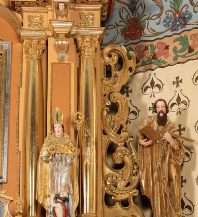 Zdjęcie nr 63: Nastawa ołtarzowa architektoniczna, jednoosiowa, jednokondygnacyjna z bramkami i zwieńczeniem, ustawiona na wysokim, dwustrefowym cokole. Ołtarz prostopadłościenny, murowany, umieszczony w drewnianej obudowie. Antependium ujęte ramą dekorowaną plecionką, podzielone na trzy pola: w środkowym płaskorzeźbione przedstawienie Ostatniej Wieczerzy według Leonarda da Vinci, a po bokach ornament roślinny o wertykalnym układzie.

Tabernakulum architektoniczne, jednokondygnacyjne, trójosiowe, ustawione na zdwojonym na cokole z dwoma zwieńczeniami na osiach skrajnych. Osie wydzielone są parami kolumn o kapitelach kompozytowych, oś środkowa wysunięta do przodu. Podpory dźwigają pełne belkowanie wyłamane na ich linii, przerwane nad polem środkowym, gdzie kolumny dźwigają przerwany półkolisty przyczółek połączony z łukiem gzymsu, nad nim ustawiona jest rzeźba Baranka leżącego na księdze z siedmioma pieczęciami. W polu środkowym dwuskrzydłowe drzwiczki do metalowego tabernakulum ujęte ramą w formie stojącego prostokąta, zamkniętego łukiem nadwieszonym z długim uskokiem. Na drzwiczkach znajdują się dwa aplikowane klęczące anioły, powyżej Chrismo w medalionie, otoczonym glorią. W osiach bocznych są nisze zamknięte konchami z figurkami aniołów, zamknięte zwieńczeniami w formie stojących prostokątów z falistym gzymsem i gałązkami lilii na szczycie; w polu srebrzone, owalne medaliony. Po bokach kondygnacji na wolutowych uszach oraz po bokach zwieńczeń znajdują się wazony ze słonecznikami. Cokół zdobiony jest ornamentem akantowym.

Kondygnacja ujęta jest dwiema parami kolumn o kapitelach kompozytowych oraz stojącą między nimi parą filarów. Podpory dźwigają pełne belkowanie o silnie wysuniętym gzymsie, wyłamane na osiach bocznych, z podwieszonymi szyszkami na tle filarów; przerwane nad polem środkowym. W centrum pole w formie stojącego prostokąta ujęte ramą dekorowaną ornamentem roślinnym z płaskorzeźbionym przedstawieniem Matki Boskiej z Dzieciątkiem. Na zasuwie obrazy: „Najświętsze Serce Pana Jezusa”, „Zwiastowanie” oraz „Św. Mikołaj”. Nad bramkami oraz pomiędzy kolumnami ustawione są rzeźby. Od lewej kolejno: św. Andrzej, św. Wojciech, św. Stanisław i na końcu po prawej św. Tomasz. Nad polem głównym znajduje się przeszklony prześwit w formie półkola z rzeźbioną gołębicą Ducha Świętego na tle glorii. Powyżej pole zamknięte półkoliście fragmentem gzymsu z rzeźbionym popiersiem błogosławiącego Boga Ojca pośród obłoków. Zwieńczenie w formie zbliżonej do stojącego prostokąta o wklęsłych bokach z gzymsem i z podwieszonym lambrekinem oraz kotarami spływającymi na boki. W polu przeszklony prześwit w formie kwadratu zamkniętego łukiem nadwieszonym z rzeźbionym monogramem Marii na tle glorii. Po bokach zwieńczenia ustawione są dwie duże figury klęczących aniołów.

Bramki po bokach ołtarza ustawione są na wysokości cokołu nastawy; przejścia ujęte są parą kanelowanych pilastrów, zamknięte łukiem utworzonym z dwóch przeciwstawnych wolut wspierających wieńczące cokoły. Przejścia w formie wydłużonego stojącego prostokąta zamkniętego łukiem półkolistym nadwieszonym.

Całość ołtarza oprócz tabernakulum dekorowana jest ornamentem małżowinowo-chrząstkowym. Uszy flankujące kondygnację utworzone są również z ornamentu małżowinowo-chrząstkowego. Na zamknięciu zwieńczenia znajdują się dwie uskrzydlone główki anielskie skierowane na wprost z podwieszonymi u szyi chustami. Struktura ołtarza polichromowana jest w kolorze brązowym ze złoconymi kolumnami, ornamentyką i profilami, detale srebrzone.