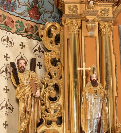 Zdjęcie nr 64: Nastawa ołtarzowa architektoniczna, jednoosiowa, jednokondygnacyjna z bramkami i zwieńczeniem, ustawiona na wysokim, dwustrefowym cokole. Ołtarz prostopadłościenny, murowany, umieszczony w drewnianej obudowie. Antependium ujęte ramą dekorowaną plecionką, podzielone na trzy pola: w środkowym płaskorzeźbione przedstawienie Ostatniej Wieczerzy według Leonarda da Vinci, a po bokach ornament roślinny o wertykalnym układzie.

Tabernakulum architektoniczne, jednokondygnacyjne, trójosiowe, ustawione na zdwojonym na cokole z dwoma zwieńczeniami na osiach skrajnych. Osie wydzielone są parami kolumn o kapitelach kompozytowych, oś środkowa wysunięta do przodu. Podpory dźwigają pełne belkowanie wyłamane na ich linii, przerwane nad polem środkowym, gdzie kolumny dźwigają przerwany półkolisty przyczółek połączony z łukiem gzymsu, nad nim ustawiona jest rzeźba Baranka leżącego na księdze z siedmioma pieczęciami. W polu środkowym dwuskrzydłowe drzwiczki do metalowego tabernakulum ujęte ramą w formie stojącego prostokąta, zamkniętego łukiem nadwieszonym z długim uskokiem. Na drzwiczkach znajdują się dwa aplikowane klęczące anioły, powyżej Chrismo w medalionie, otoczonym glorią. W osiach bocznych są nisze zamknięte konchami z figurkami aniołów, zamknięte zwieńczeniami w formie stojących prostokątów z falistym gzymsem i gałązkami lilii na szczycie; w polu srebrzone, owalne medaliony. Po bokach kondygnacji na wolutowych uszach oraz po bokach zwieńczeń znajdują się wazony ze słonecznikami. Cokół zdobiony jest ornamentem akantowym.

Kondygnacja ujęta jest dwiema parami kolumn o kapitelach kompozytowych oraz stojącą między nimi parą filarów. Podpory dźwigają pełne belkowanie o silnie wysuniętym gzymsie, wyłamane na osiach bocznych, z podwieszonymi szyszkami na tle filarów; przerwane nad polem środkowym. W centrum pole w formie stojącego prostokąta ujęte ramą dekorowaną ornamentem roślinnym z płaskorzeźbionym przedstawieniem Matki Boskiej z Dzieciątkiem. Na zasuwie obrazy: „Najświętsze Serce Pana Jezusa”, „Zwiastowanie” oraz „Św. Mikołaj”. Nad bramkami oraz pomiędzy kolumnami ustawione są rzeźby. Od lewej kolejno: św. Andrzej, św. Wojciech, św. Stanisław i na końcu po prawej św. Tomasz. Nad polem głównym znajduje się przeszklony prześwit w formie półkola z rzeźbioną gołębicą Ducha Świętego na tle glorii. Powyżej pole zamknięte półkoliście fragmentem gzymsu z rzeźbionym popiersiem błogosławiącego Boga Ojca pośród obłoków. Zwieńczenie w formie zbliżonej do stojącego prostokąta o wklęsłych bokach z gzymsem i z podwieszonym lambrekinem oraz kotarami spływającymi na boki. W polu przeszklony prześwit w formie kwadratu zamkniętego łukiem nadwieszonym z rzeźbionym monogramem Marii na tle glorii. Po bokach zwieńczenia ustawione są dwie duże figury klęczących aniołów.

Bramki po bokach ołtarza ustawione są na wysokości cokołu nastawy; przejścia ujęte są parą kanelowanych pilastrów, zamknięte łukiem utworzonym z dwóch przeciwstawnych wolut wspierających wieńczące cokoły. Przejścia w formie wydłużonego stojącego prostokąta zamkniętego łukiem półkolistym nadwieszonym.

Całość ołtarza oprócz tabernakulum dekorowana jest ornamentem małżowinowo-chrząstkowym. Uszy flankujące kondygnację utworzone są również z ornamentu małżowinowo-chrząstkowego. Na zamknięciu zwieńczenia znajdują się dwie uskrzydlone główki anielskie skierowane na wprost z podwieszonymi u szyi chustami. Struktura ołtarza polichromowana jest w kolorze brązowym ze złoconymi kolumnami, ornamentyką i profilami, detale srebrzone.