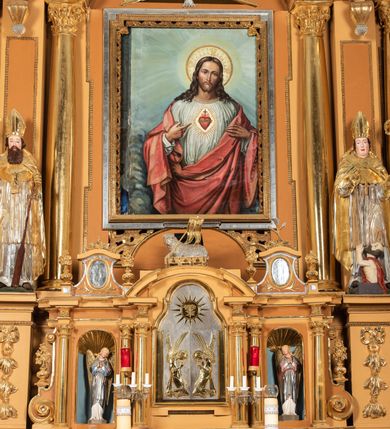 Zdjęcie nr 37: Nastawa ołtarzowa architektoniczna, jednoosiowa, jednokondygnacyjna z bramkami i zwieńczeniem, ustawiona na wysokim, dwustrefowym cokole. Ołtarz prostopadłościenny, murowany, umieszczony w drewnianej obudowie. Antependium ujęte ramą dekorowaną plecionką, podzielone na trzy pola: w środkowym płaskorzeźbione przedstawienie Ostatniej Wieczerzy według Leonarda da Vinci, a po bokach ornament roślinny o wertykalnym układzie.

Tabernakulum architektoniczne, jednokondygnacyjne, trójosiowe, ustawione na zdwojonym na cokole z dwoma zwieńczeniami na osiach skrajnych. Osie wydzielone są parami kolumn o kapitelach kompozytowych, oś środkowa wysunięta do przodu. Podpory dźwigają pełne belkowanie wyłamane na ich linii, przerwane nad polem środkowym, gdzie kolumny dźwigają przerwany półkolisty przyczółek połączony z łukiem gzymsu, nad nim ustawiona jest rzeźba Baranka leżącego na księdze z siedmioma pieczęciami. W polu środkowym dwuskrzydłowe drzwiczki do metalowego tabernakulum ujęte ramą w formie stojącego prostokąta, zamkniętego łukiem nadwieszonym z długim uskokiem. Na drzwiczkach znajdują się dwa aplikowane klęczące anioły, powyżej Chrismo w medalionie, otoczonym glorią. W osiach bocznych są nisze zamknięte konchami z figurkami aniołów, zamknięte zwieńczeniami w formie stojących prostokątów z falistym gzymsem i gałązkami lilii na szczycie; w polu srebrzone, owalne medaliony. Po bokach kondygnacji na wolutowych uszach oraz po bokach zwieńczeń znajdują się wazony ze słonecznikami. Cokół zdobiony jest ornamentem akantowym.

Kondygnacja ujęta jest dwiema parami kolumn o kapitelach kompozytowych oraz stojącą między nimi parą filarów. Podpory dźwigają pełne belkowanie o silnie wysuniętym gzymsie, wyłamane na osiach bocznych, z podwieszonymi szyszkami na tle filarów; przerwane nad polem środkowym. W centrum pole w formie stojącego prostokąta ujęte ramą dekorowaną ornamentem roślinnym z płaskorzeźbionym przedstawieniem Matki Boskiej z Dzieciątkiem. Na zasuwie obrazy: „Najświętsze Serce Pana Jezusa”, „Zwiastowanie” oraz „Św. Mikołaj”. Nad bramkami oraz pomiędzy kolumnami ustawione są rzeźby. Od lewej kolejno: św. Andrzej, św. Wojciech, św. Stanisław i na końcu po prawej św. Tomasz. Nad polem głównym znajduje się przeszklony prześwit w formie półkola z rzeźbioną gołębicą Ducha Świętego na tle glorii. Powyżej pole zamknięte półkoliście fragmentem gzymsu z rzeźbionym popiersiem błogosławiącego Boga Ojca pośród obłoków. Zwieńczenie w formie zbliżonej do stojącego prostokąta o wklęsłych bokach z gzymsem i z podwieszonym lambrekinem oraz kotarami spływającymi na boki. W polu przeszklony prześwit w formie kwadratu zamkniętego łukiem nadwieszonym z rzeźbionym monogramem Marii na tle glorii. Po bokach zwieńczenia ustawione są dwie duże figury klęczących aniołów.

Bramki po bokach ołtarza ustawione są na wysokości cokołu nastawy; przejścia ujęte są parą kanelowanych pilastrów, zamknięte łukiem utworzonym z dwóch przeciwstawnych wolut wspierających wieńczące cokoły. Przejścia w formie wydłużonego stojącego prostokąta zamkniętego łukiem półkolistym nadwieszonym.

Całość ołtarza oprócz tabernakulum dekorowana jest ornamentem małżowinowo-chrząstkowym. Uszy flankujące kondygnację utworzone są również z ornamentu małżowinowo-chrząstkowego. Na zamknięciu zwieńczenia znajdują się dwie uskrzydlone główki anielskie skierowane na wprost z podwieszonymi u szyi chustami. Struktura ołtarza polichromowana jest w kolorze brązowym ze złoconymi kolumnami, ornamentyką i profilami, detale srebrzone.