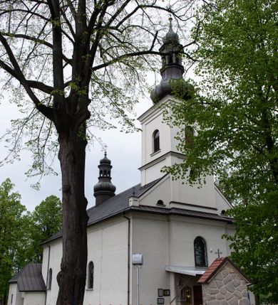 Zdjęcie nr 1: Kościół usytuowany jest w południowo-wschodniej części wsi, otoczony kamiennym murem, otynkowanym, krytym betonową płytą, w który wbudowano współczesne stacje drogi krzyżowej. Na plac kościelny prowadzą trzy bramy. Główna brama znajduje się w murze od strony zachodniej, nakryta jest ostrołukową arkadą. Dwie mniejsze bramy zlokalizowane są od strony południowej oraz od strony wschodniej. Na placu przed kościołem stoi pomnik z 1911 roku wystawiony na pamiątkę księdza Wojciecha Blaszyńskiego i działacza ludowego Stanisława Stojałowskiego. 
Świątynia jest orientowana, murowana, jednonawowa z węższym i krótkim prezbiterium, zamkniętym półkoliście oraz z wieżą na zakończeniu nawy. Do prezbiterium przylega zakrystia od północy i skarbczyk od południa. Od strony południowej dobudowana jest również niska kruchta. Wnętrze trójprzęsłowej nawy rozczłonkowane jest filarami przyściennymi wspierającymi sklepienie żagielkowe. Chór muzyczny trójarkadowy, wsparty na dwóch filarach. W ścianach korpusu nawowego znajdują się głębokie wnęki, w których umieszczone są prostokątne otwory okienne zamknięte półkolistym łukiem, po trzy od strony północnej i południowej; takie same okno znajduje się również w apsydzie od strony południowej oraz na chórze od strony zachodniej. Ponadto w apsydzie na wysokości zwieńczenia ołtarza głównego umieszczone jest małe, okrągłe okno. W kruchcie, skarbczyku i zakrystii okna są prostokątne. Drzwi główne dwuskrzydłowe, drewniane z metalowymi okuciami, zabezpieczone od wewnątrz dwiema żelaznymi zaporami umocowanymi w murze. Podobne drzwi znajdują się od strony południowej z kruchty. 
Fasada kościoła jest płaska, zakończona gzymsem z wysuniętą do przodu trójkondygnacyjną wieżą, nakrytą baniastym hełmem z latarnią. Drugie piętro wieży połączone jest z fasadą prostymi spływami. Przy wejściu na wysokich cokołach ustawione są rzeźby świętych Piotra i Pawła. 
Kościoł nakryty jest dachem dwuspadowym, na skrzyżowaniu nawy z prezbiterium umieszczona jest sygnaturka z hełmem baniastym z latarnią. 
