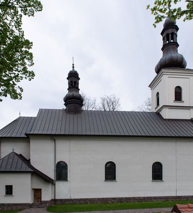 Zdjęcie nr 6: Kościół usytuowany jest w południowo-wschodniej części wsi, otoczony kamiennym murem, otynkowanym, krytym betonową płytą, w który wbudowano współczesne stacje drogi krzyżowej. Na plac kościelny prowadzą trzy bramy. Główna brama znajduje się w murze od strony zachodniej, nakryta jest ostrołukową arkadą. Dwie mniejsze bramy zlokalizowane są od strony południowej oraz od strony wschodniej. Na placu przed kościołem stoi pomnik z 1911 roku wystawiony na pamiątkę księdza Wojciecha Blaszyńskiego i działacza ludowego Stanisława Stojałowskiego. 
Świątynia jest orientowana, murowana, jednonawowa z węższym i krótkim prezbiterium, zamkniętym półkoliście oraz z wieżą na zakończeniu nawy. Do prezbiterium przylega zakrystia od północy i skarbczyk od południa. Od strony południowej dobudowana jest również niska kruchta. Wnętrze trójprzęsłowej nawy rozczłonkowane jest filarami przyściennymi wspierającymi sklepienie żagielkowe. Chór muzyczny trójarkadowy, wsparty na dwóch filarach. W ścianach korpusu nawowego znajdują się głębokie wnęki, w których umieszczone są prostokątne otwory okienne zamknięte półkolistym łukiem, po trzy od strony północnej i południowej; takie same okno znajduje się również w apsydzie od strony południowej oraz na chórze od strony zachodniej. Ponadto w apsydzie na wysokości zwieńczenia ołtarza głównego umieszczone jest małe, okrągłe okno. W kruchcie, skarbczyku i zakrystii okna są prostokątne. Drzwi główne dwuskrzydłowe, drewniane z metalowymi okuciami, zabezpieczone od wewnątrz dwiema żelaznymi zaporami umocowanymi w murze. Podobne drzwi znajdują się od strony południowej z kruchty. 
Fasada kościoła jest płaska, zakończona gzymsem z wysuniętą do przodu trójkondygnacyjną wieżą, nakrytą baniastym hełmem z latarnią. Drugie piętro wieży połączone jest z fasadą prostymi spływami. Przy wejściu na wysokich cokołach ustawione są rzeźby świętych Piotra i Pawła. 
Kościoł nakryty jest dachem dwuspadowym, na skrzyżowaniu nawy z prezbiterium umieszczona jest sygnaturka z hełmem baniastym z latarnią. 
